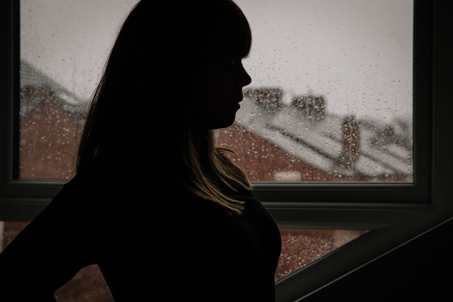A silhouette of a woman by a window looking out during sunset.