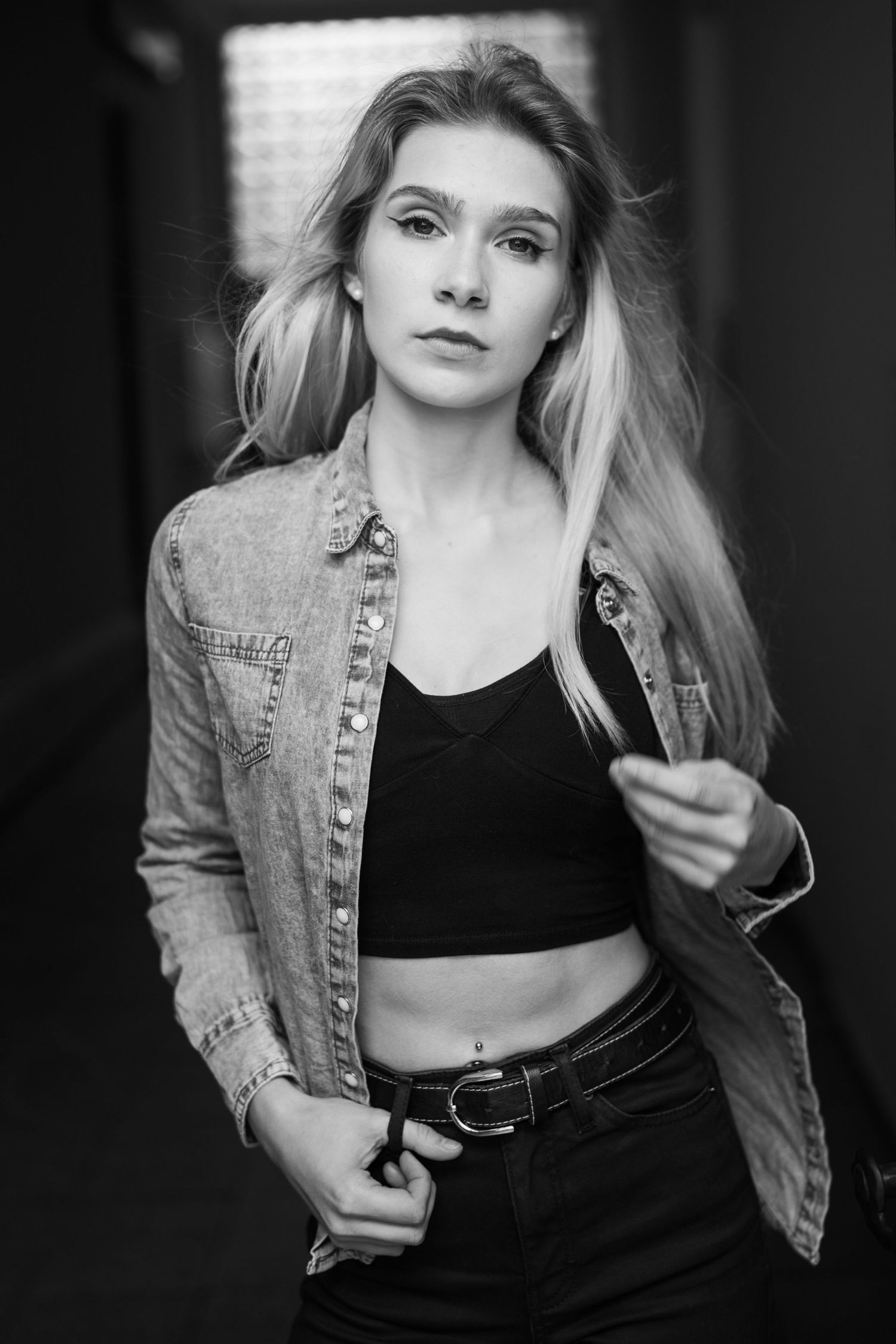 Schwarz-Weiß-Porträt einer Frau mit Jeansjacke und bauchfreiem Top und langen blonden Haaren.