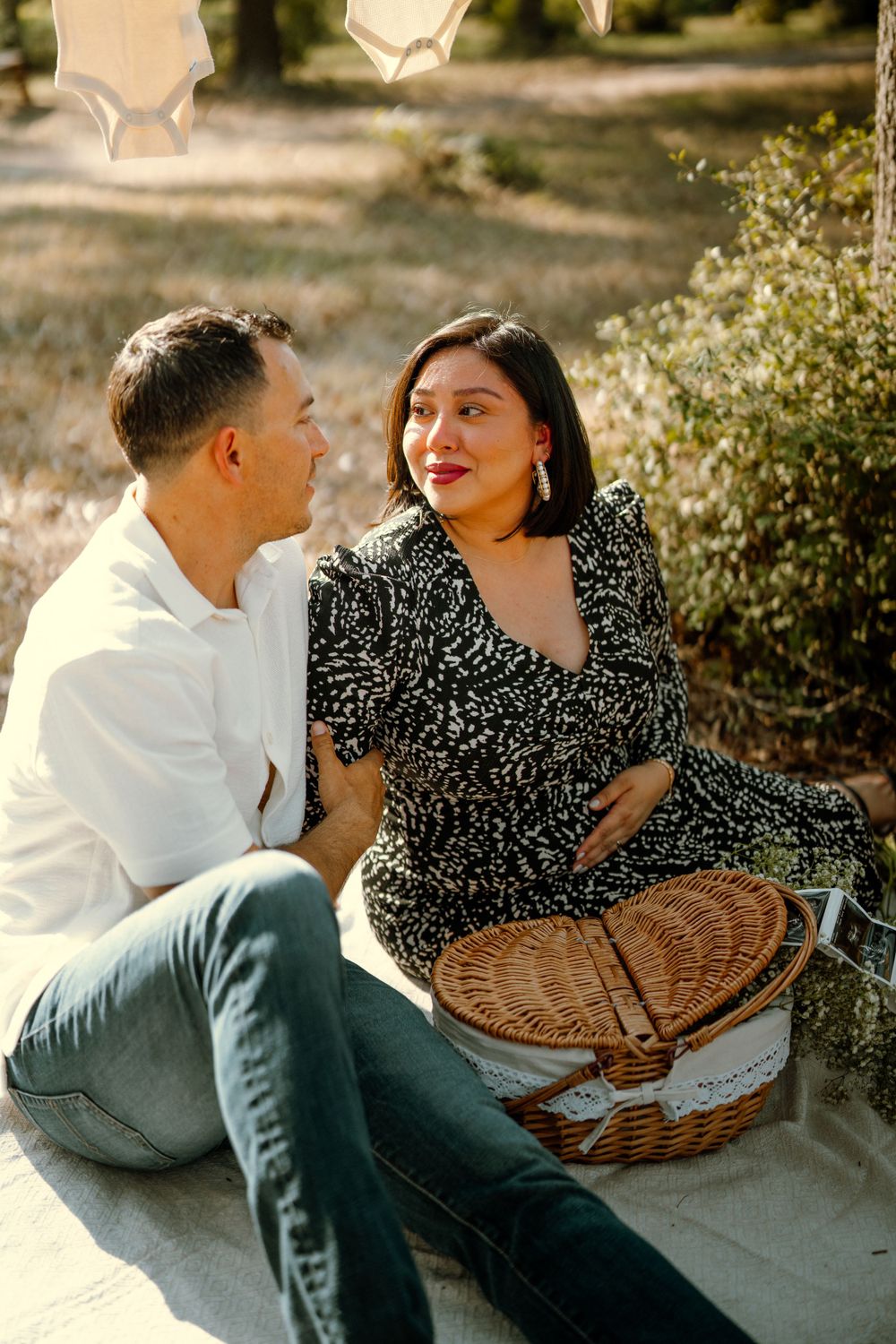 A couple sits together on a picnic blanket in golden sunlight with a wicker basket beside them.