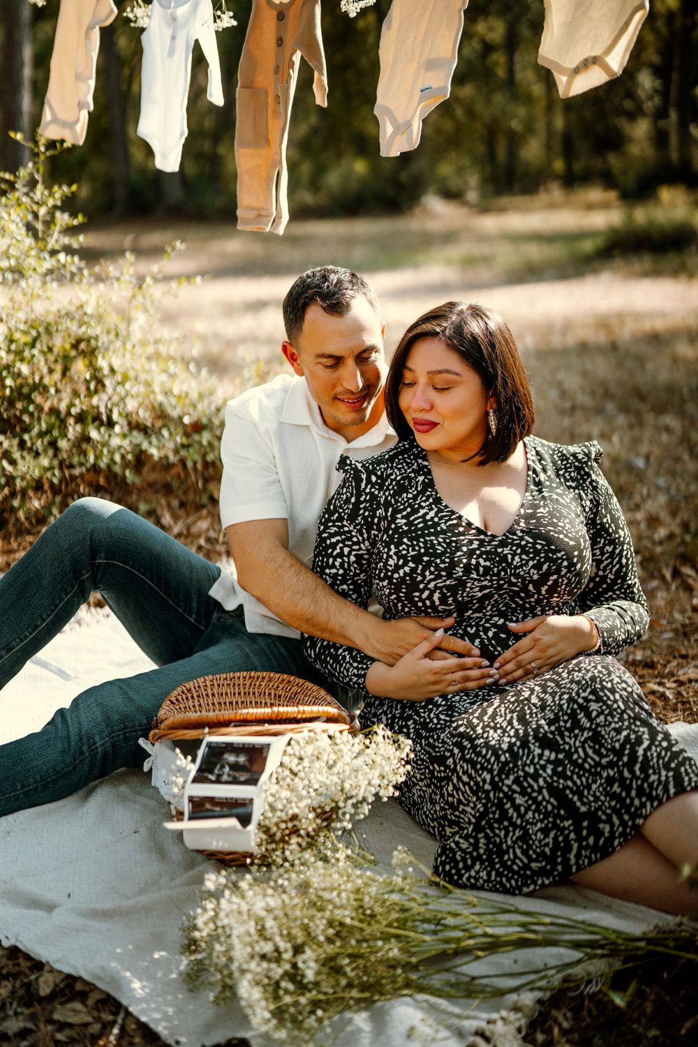 Couple sits on blanket with picnic basket and baby's breath flowers while clothes dry on line above in golden sunlight.