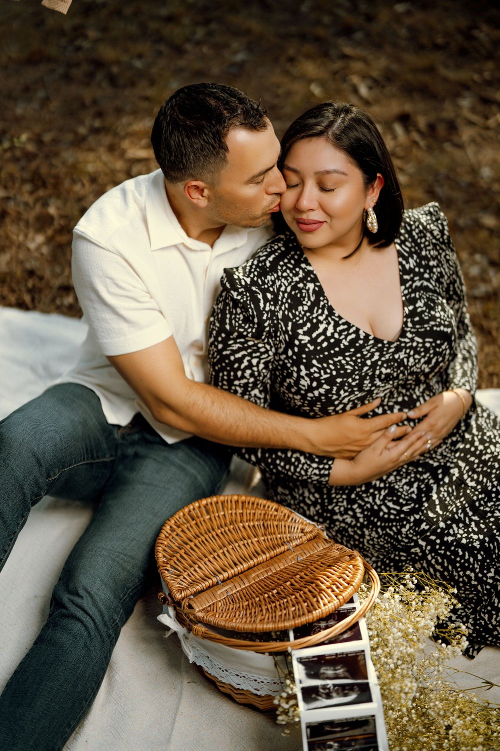 Romantic couple shares intimate moment on picnic blanket with wicker basket and dried flowers in outdoor setting.