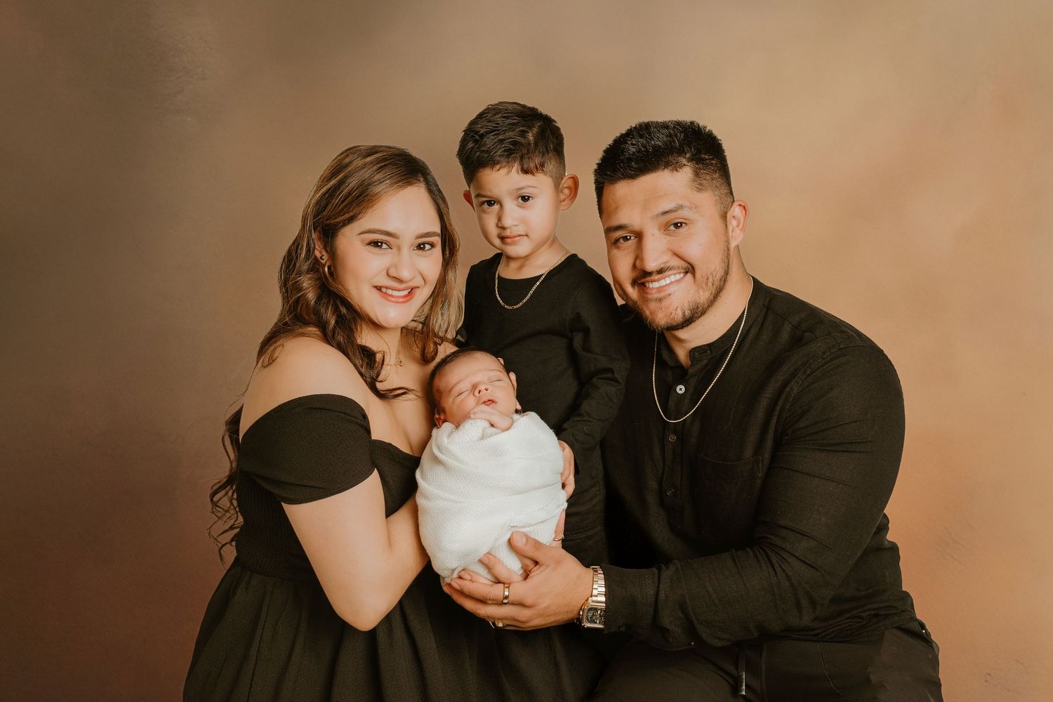 Family portrait with two adults and two children in formal black and white attire against brown backdrop.