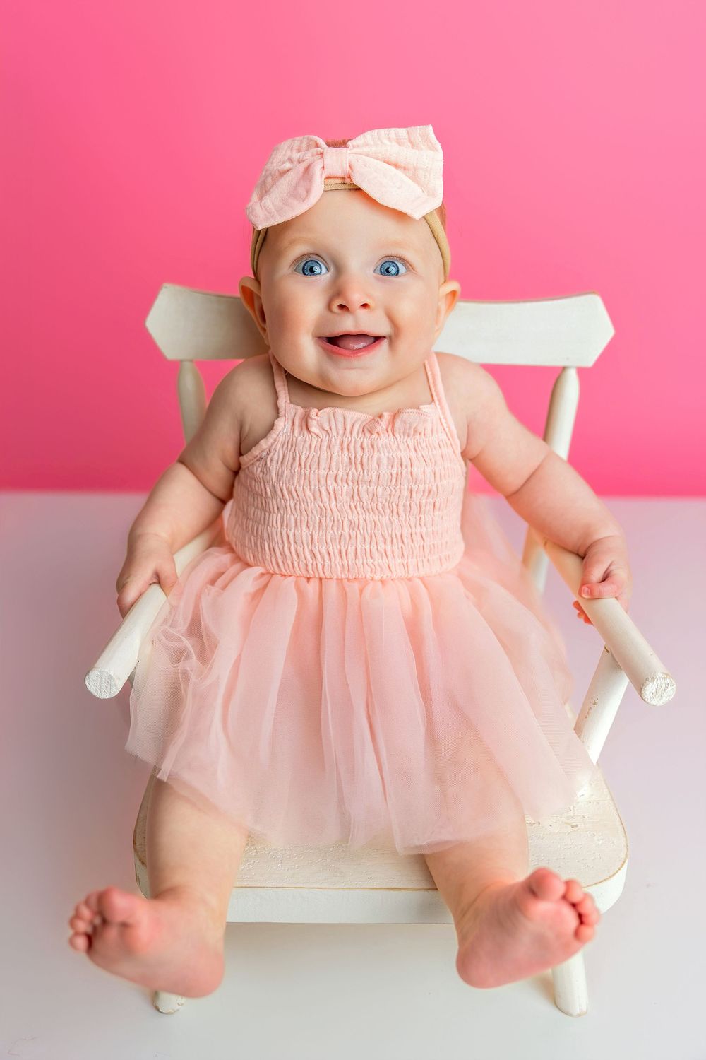 Baby wearing pink tulle dress and bow headband poses on white background against pink wall in various sitting positions.