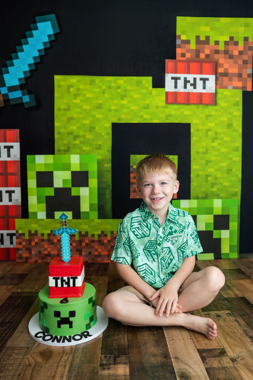 Boy smiling at Minecraft-themed birthday party with TNT cake reading Connor, surrounded by Creeper decorations.