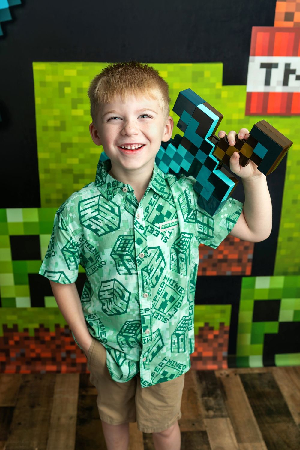 Smiling boy in Minecraft shirt holding diamond sword toy at themed birthday party.