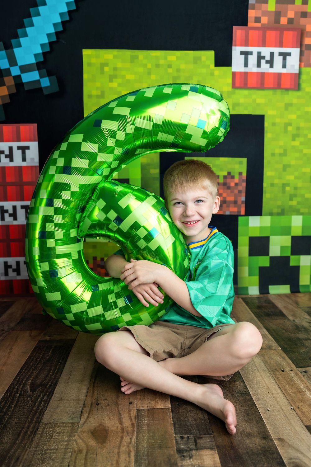 Smiling boy hugging a green number 6 balloon at a Minecraft-themed birthday party with TNT block decorations.
