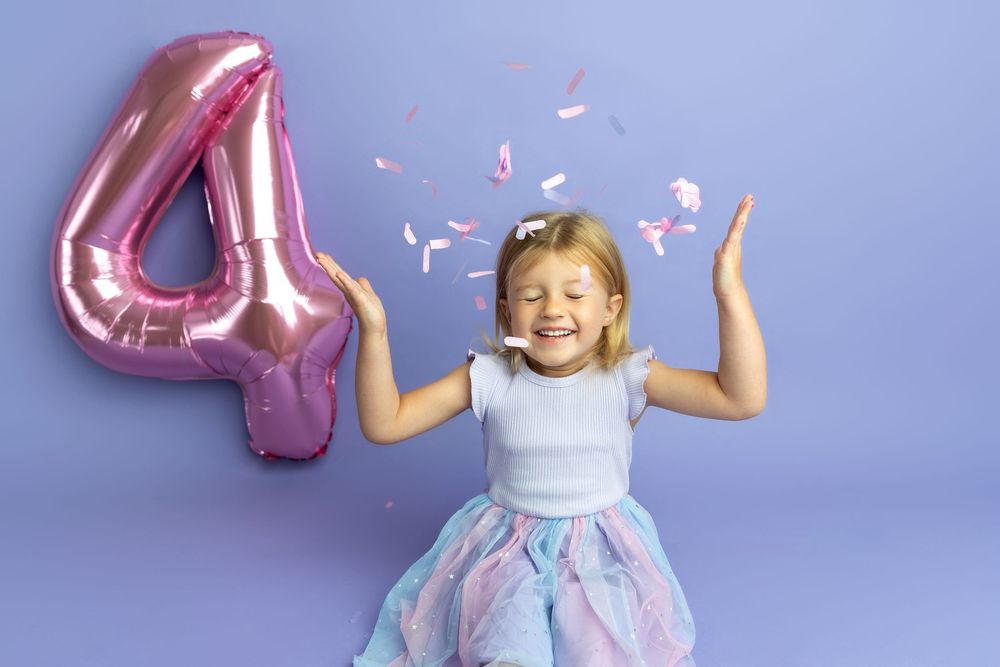 A joyful girl celebrates her 4th birthday with a pink number balloon and confetti on a purple background.