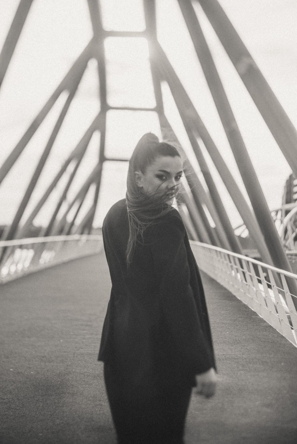 Dramatic black and white photo of a person walking across a geometric bridge structure.