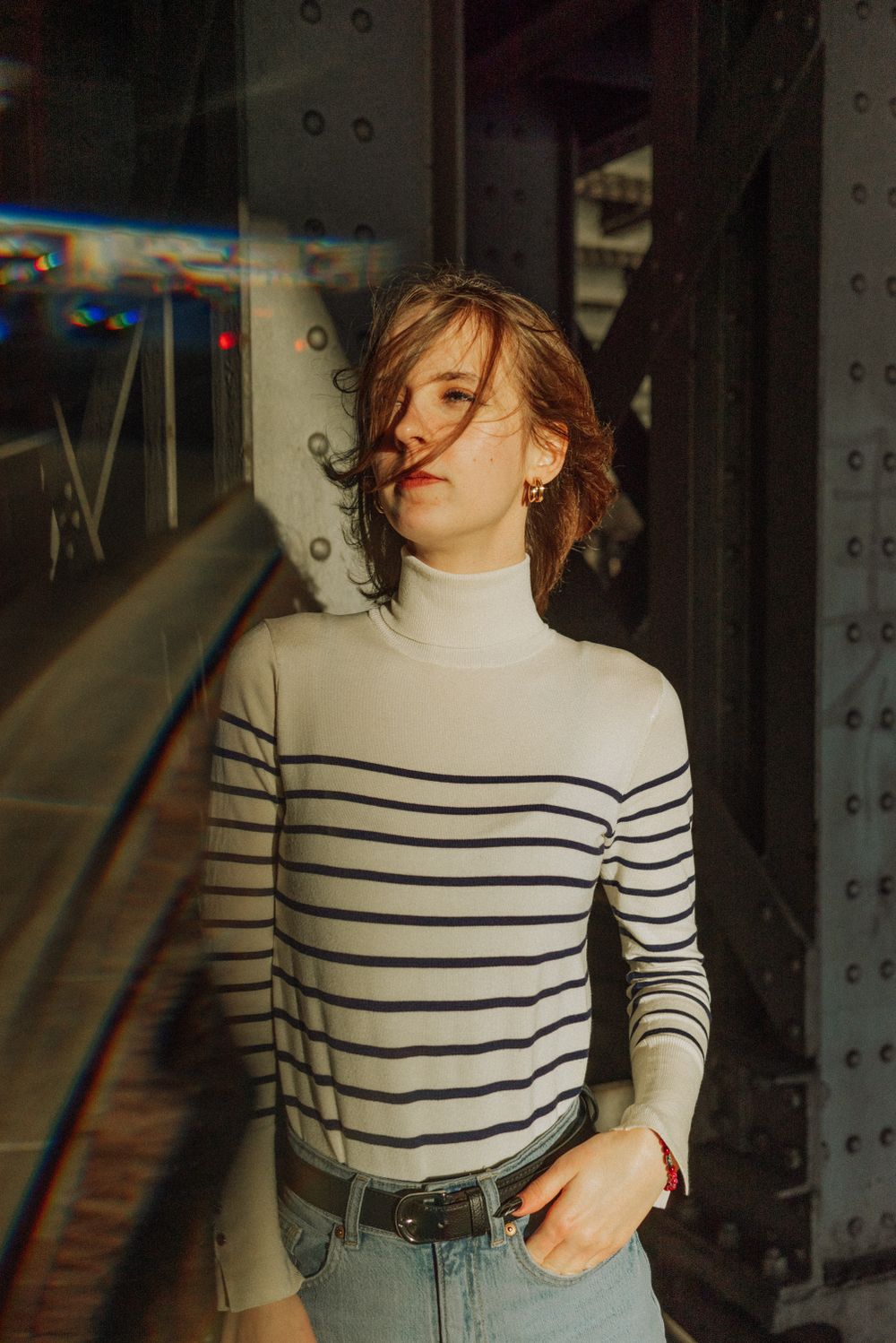 Person wearing striped turtleneck sweater poses against industrial background.