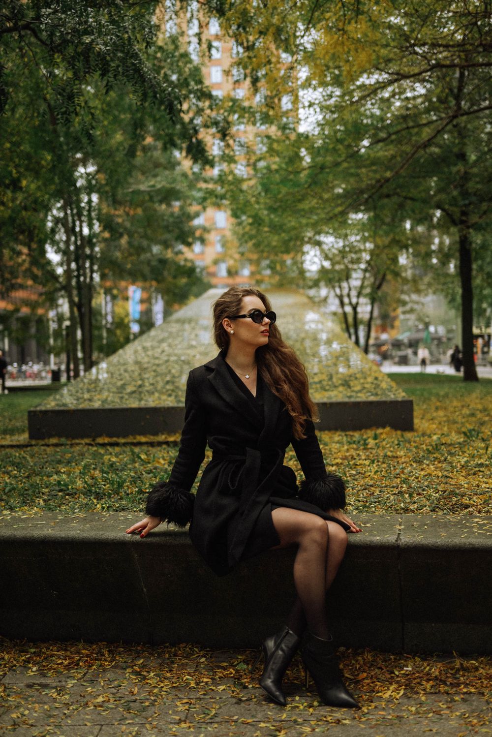 Person in dark outfit sitting on wall surrounded by autumn foliage.