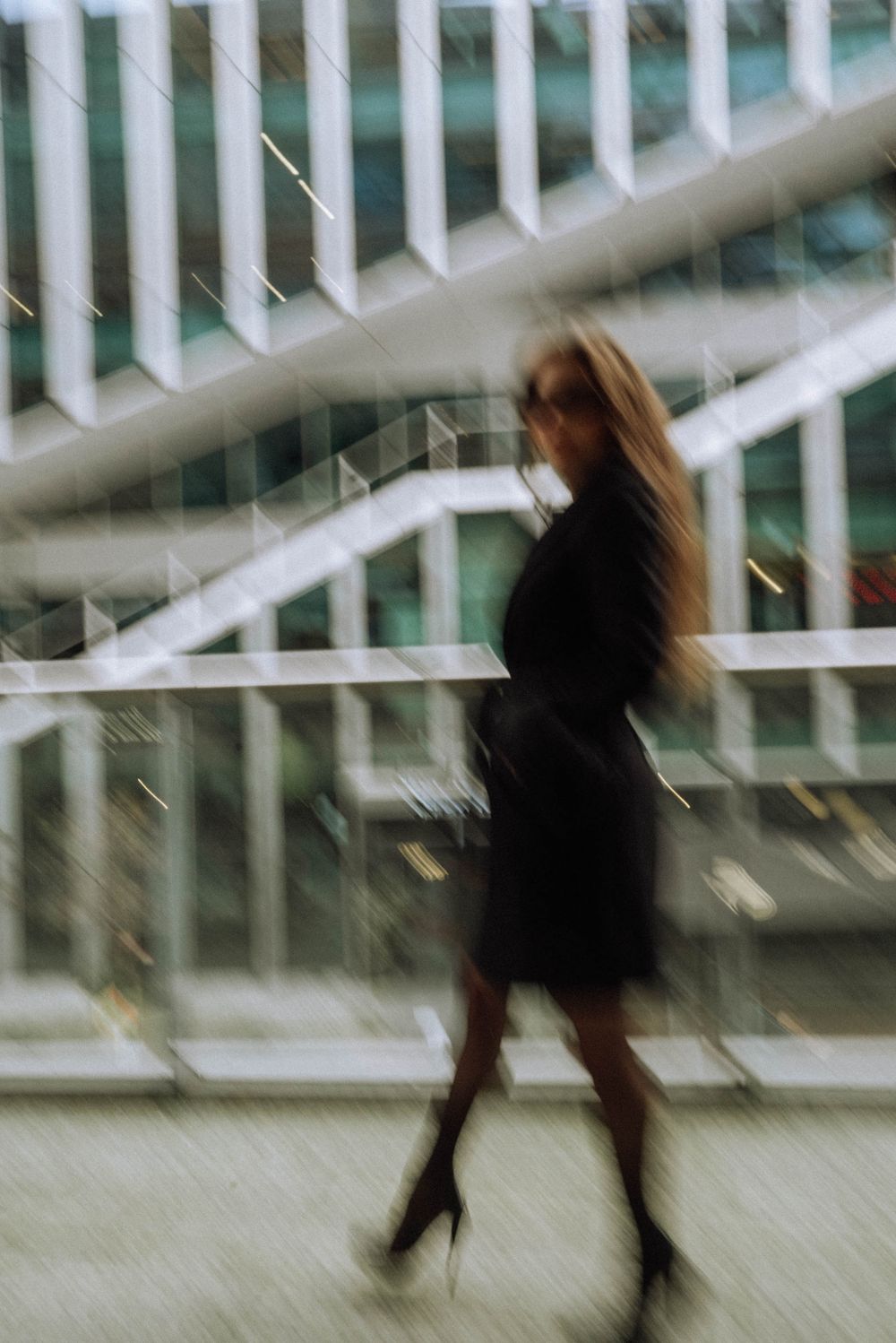 Blurred motion shot of person in black moving through modern building corridor.