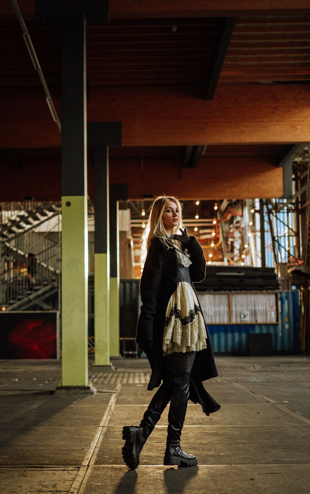 Person in black outfit dancing in an industrial indoor space with wooden ceiling.