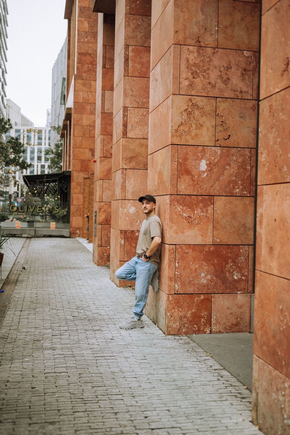 Figure in casual wear poses against orange stone architecture and cobblestone ground.