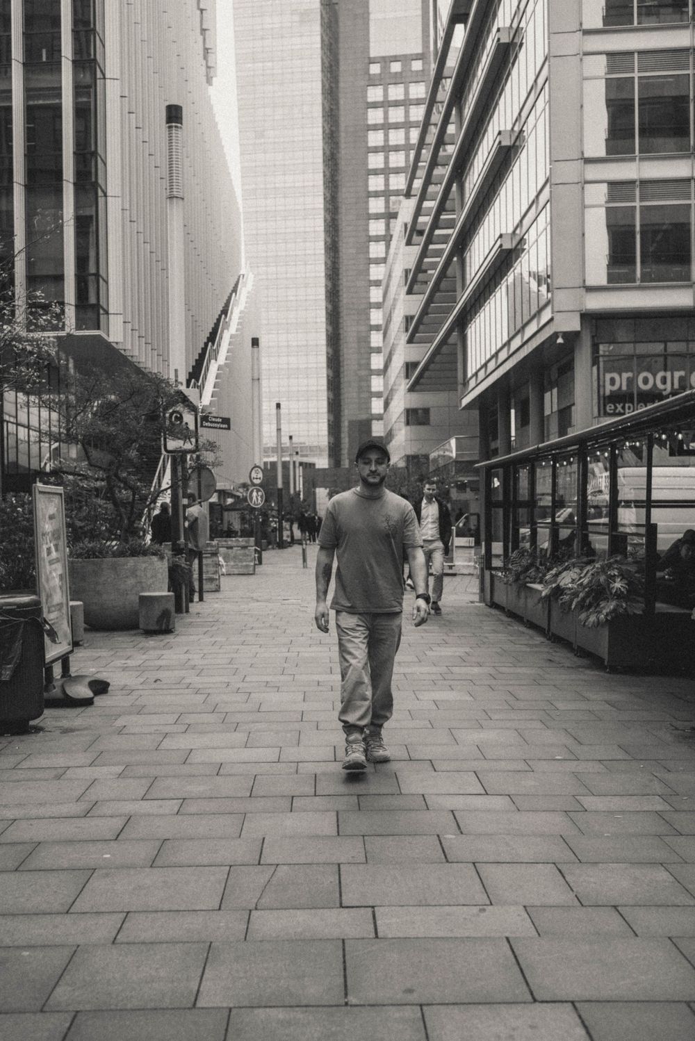 Wide angle street view of person walking on stone pavement between modern buildings.