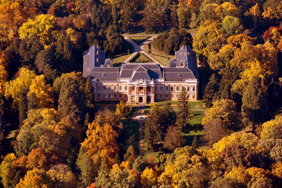 Aerial view of a historic mansion surrounded by vibrant autumn trees with golden yellow and orange foliage.