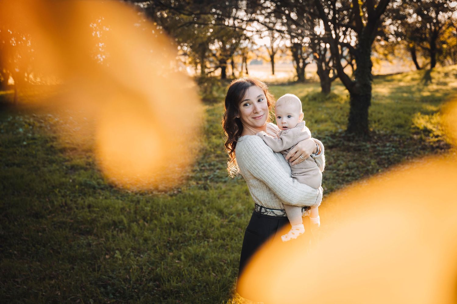 Una calda sessione fotografica di famiglia al tramonto in un parco con foglie autunnali che creano effetti bokeh dorati in primo piano.