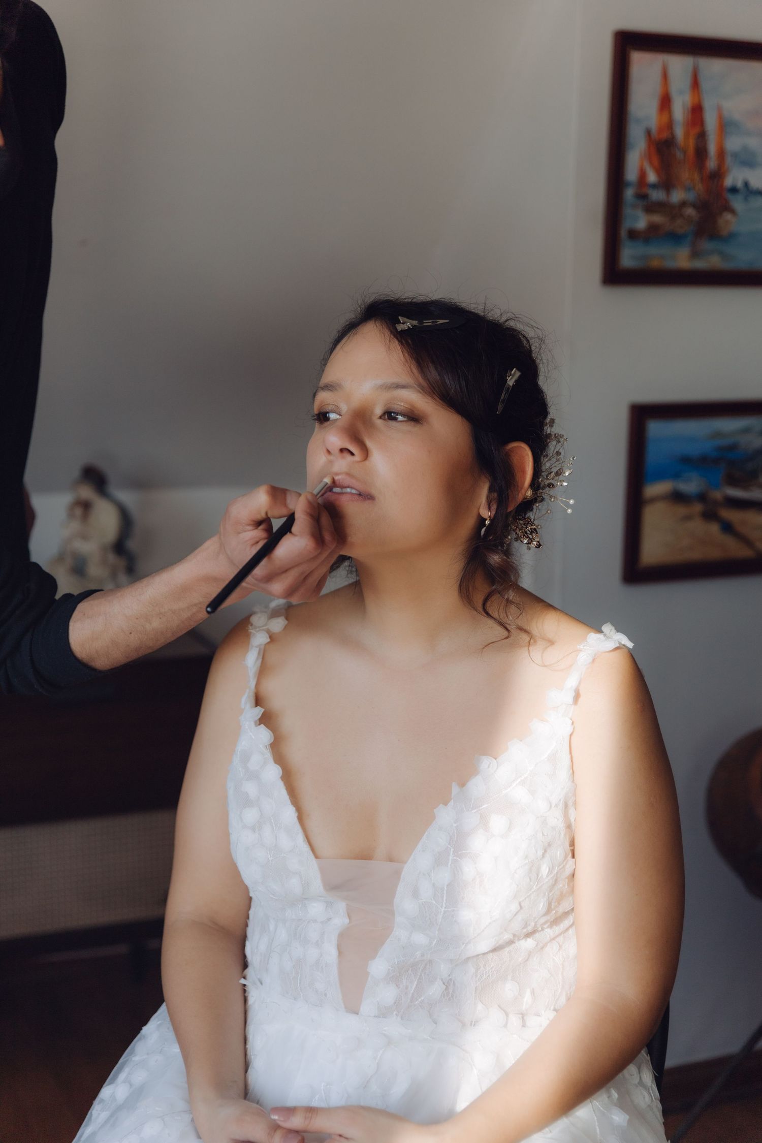Bride in white lace wedding dress getting makeup applied by artist during bridal preparation.