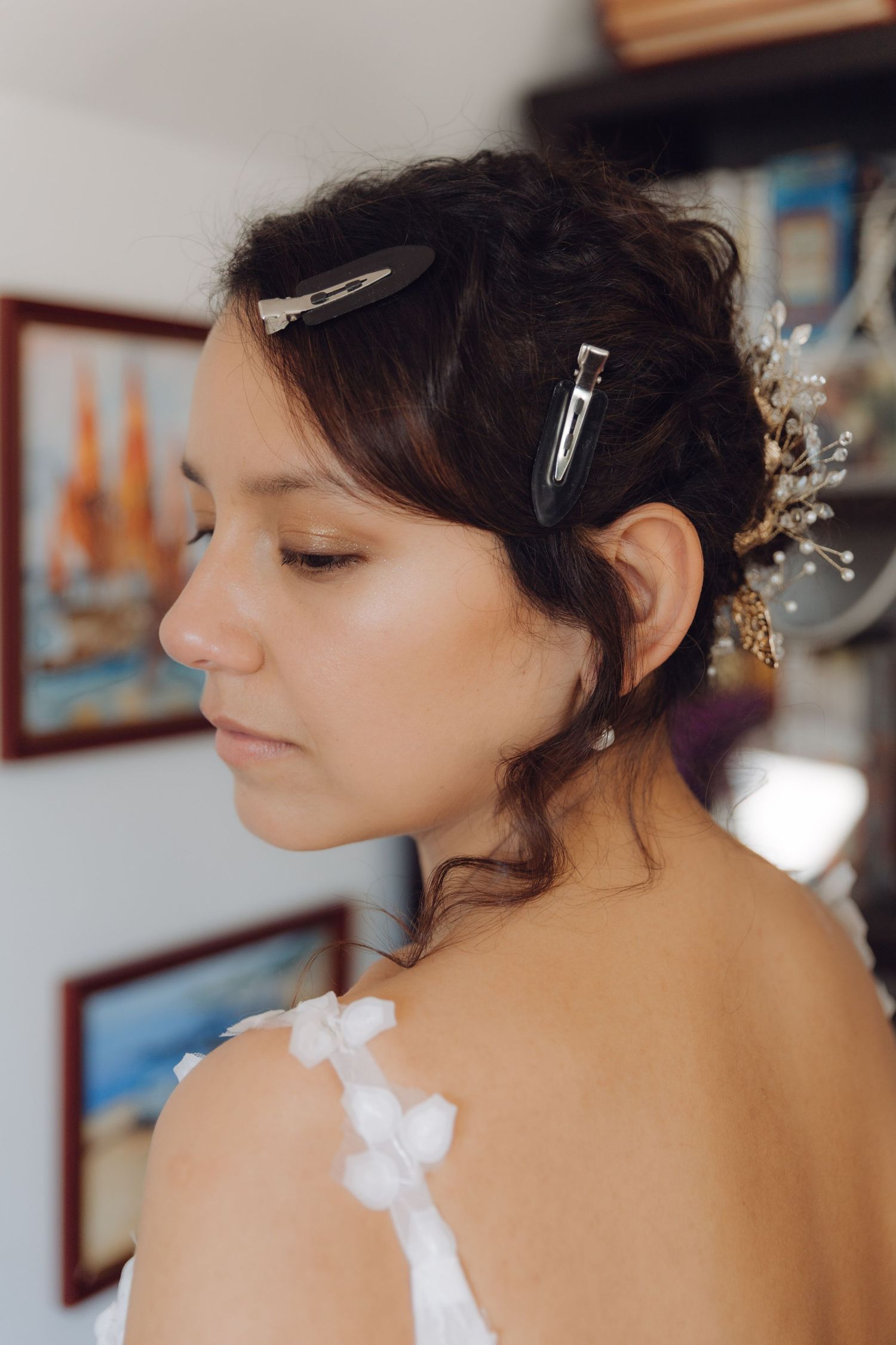 Bride in white wedding dress with elegant updo and floral hair accessories during bridal preparation.