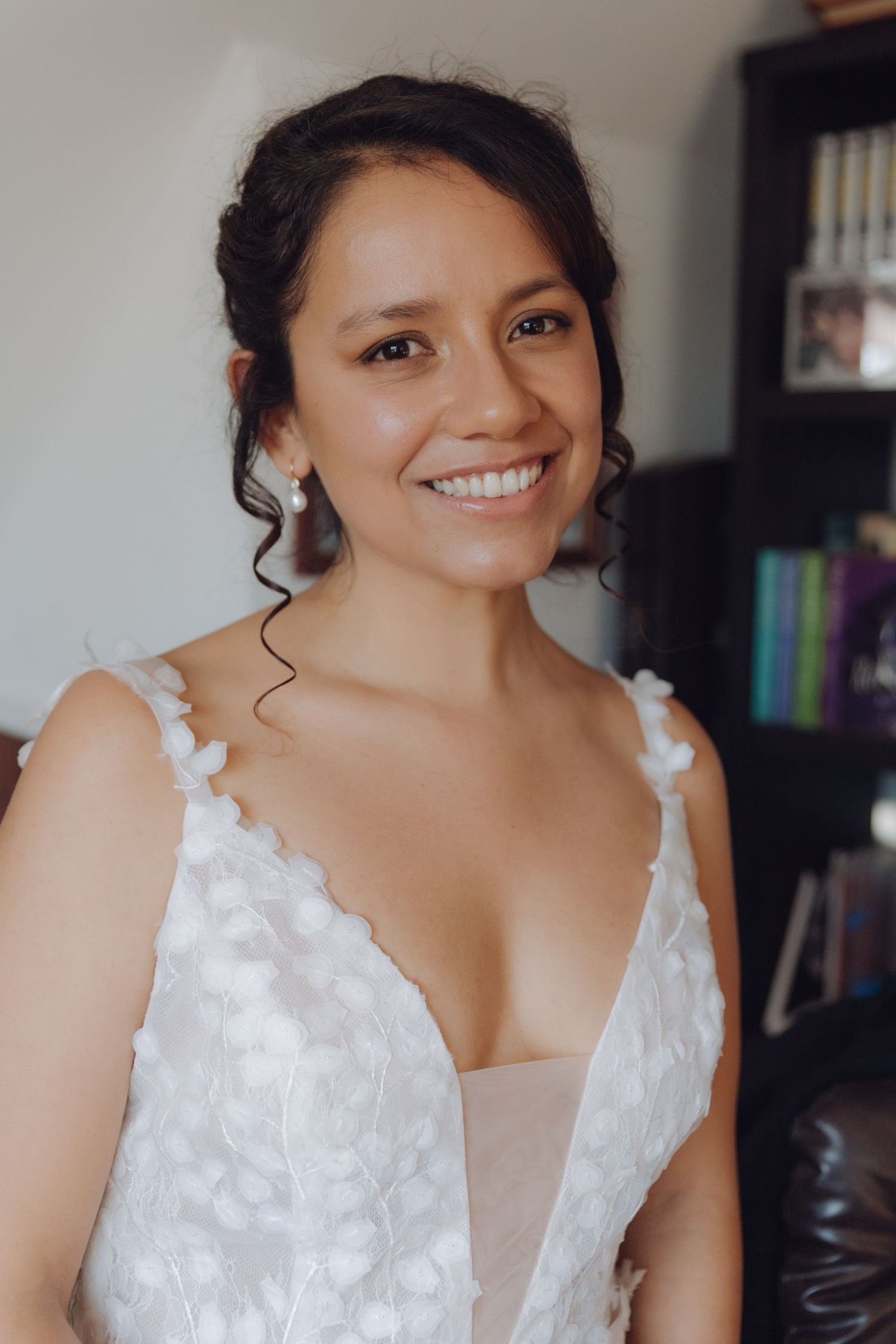 Smiling bride in a white floral applique wedding dress with deep V-neckline poses indoors.