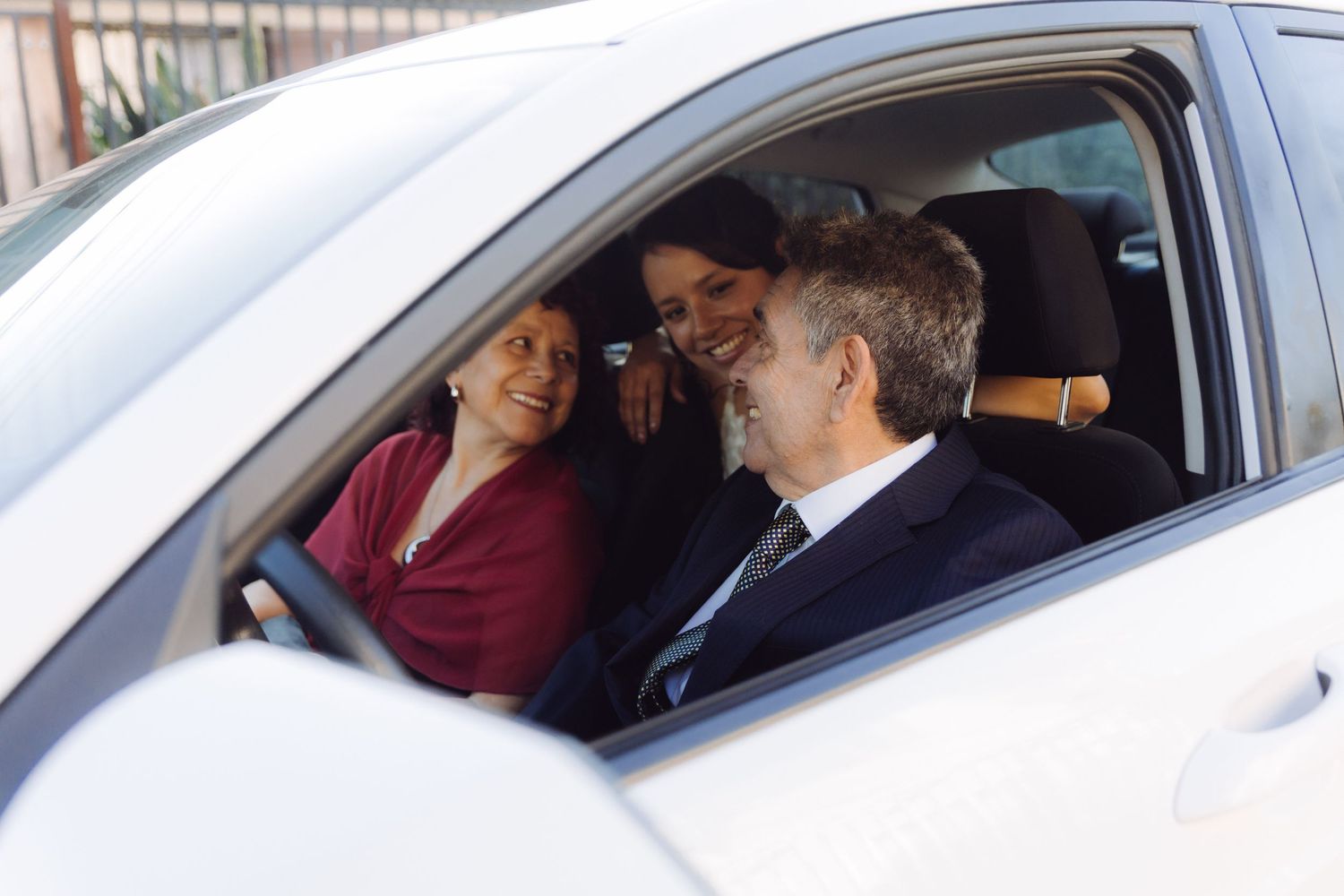 Bride and two guests share a joyful moment inside a white car before the wedding ceremony.