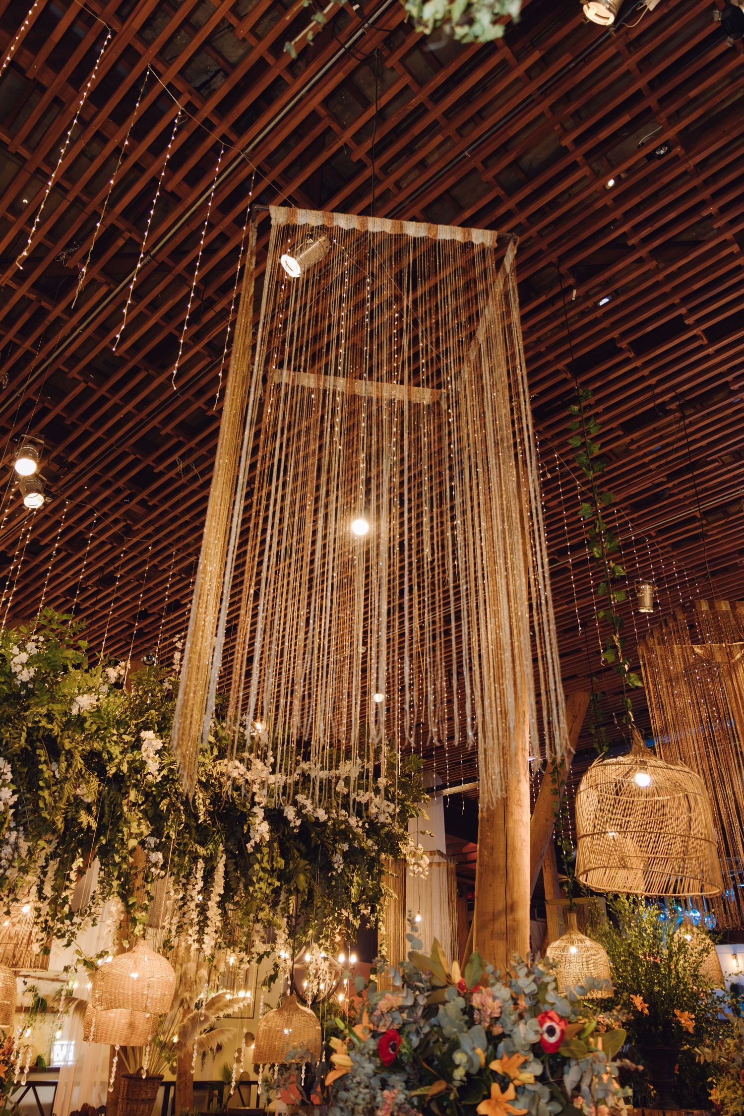 Dramatic wedding venue ceiling with cascading bead curtains, woven lanterns, and lush greenery installations.
