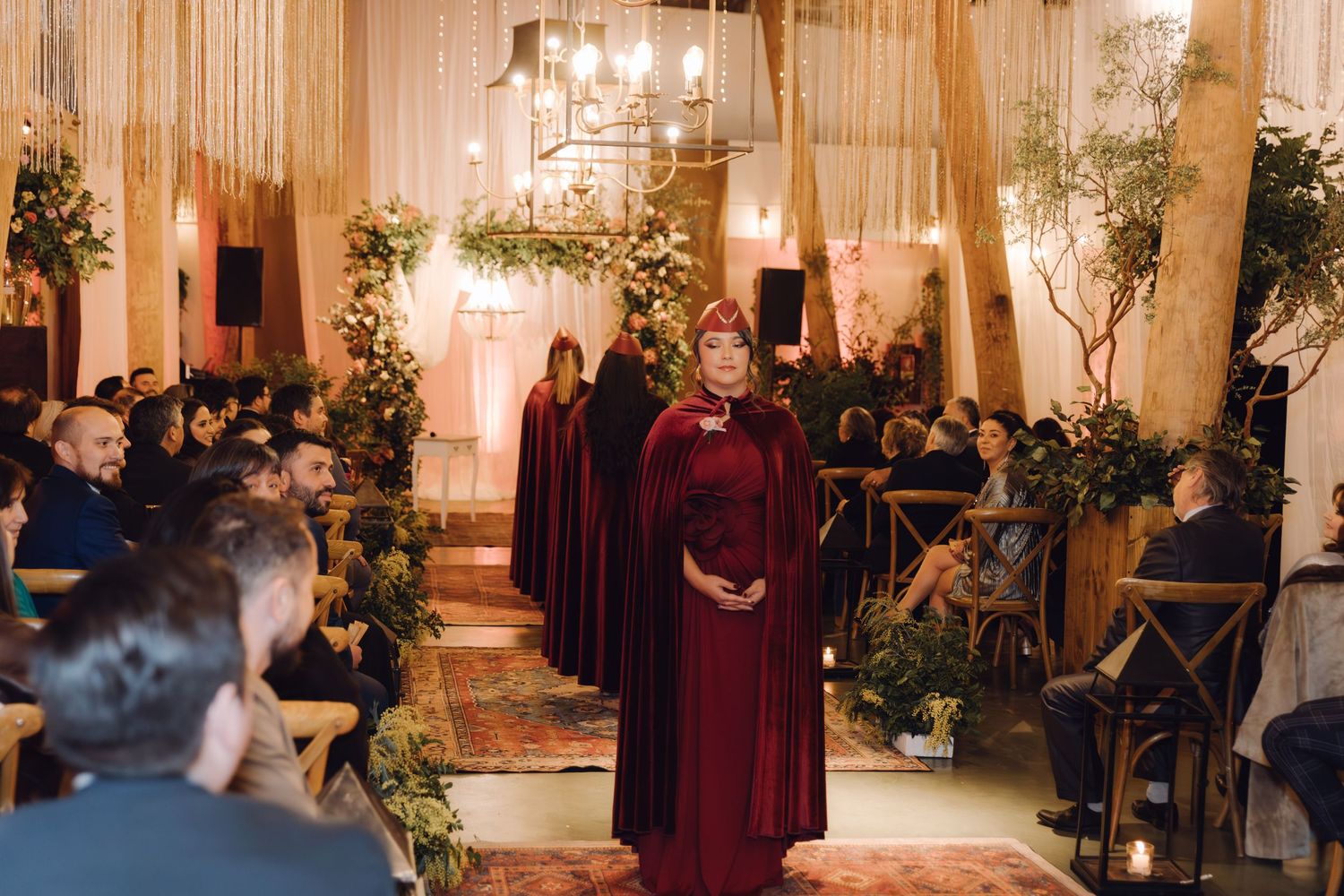 Bridesmaid in burgundy gown walking down decorated wedding aisle during ceremony.