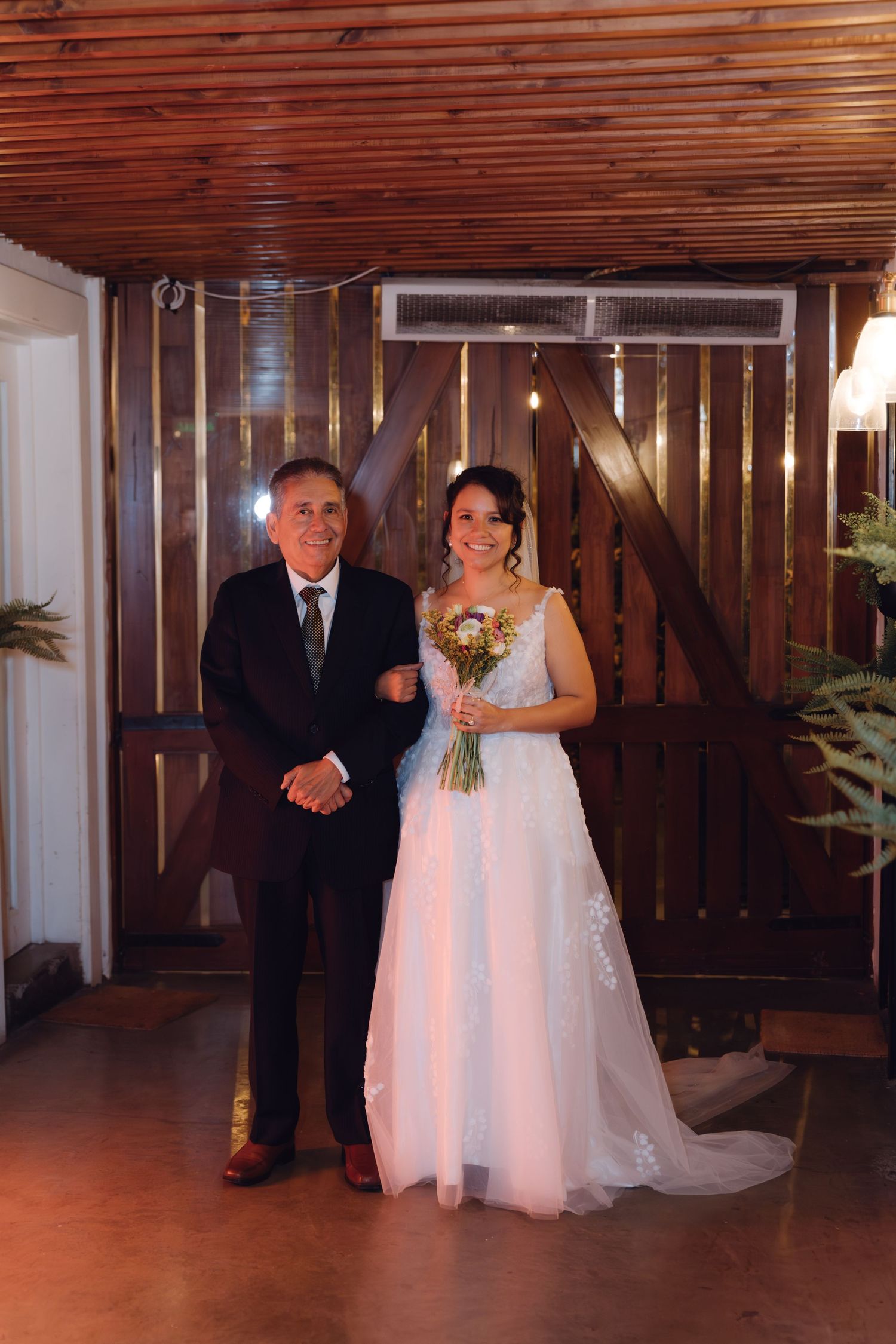 Bride in white gown holding bouquet stands with older gentleman before walking down aisle.
