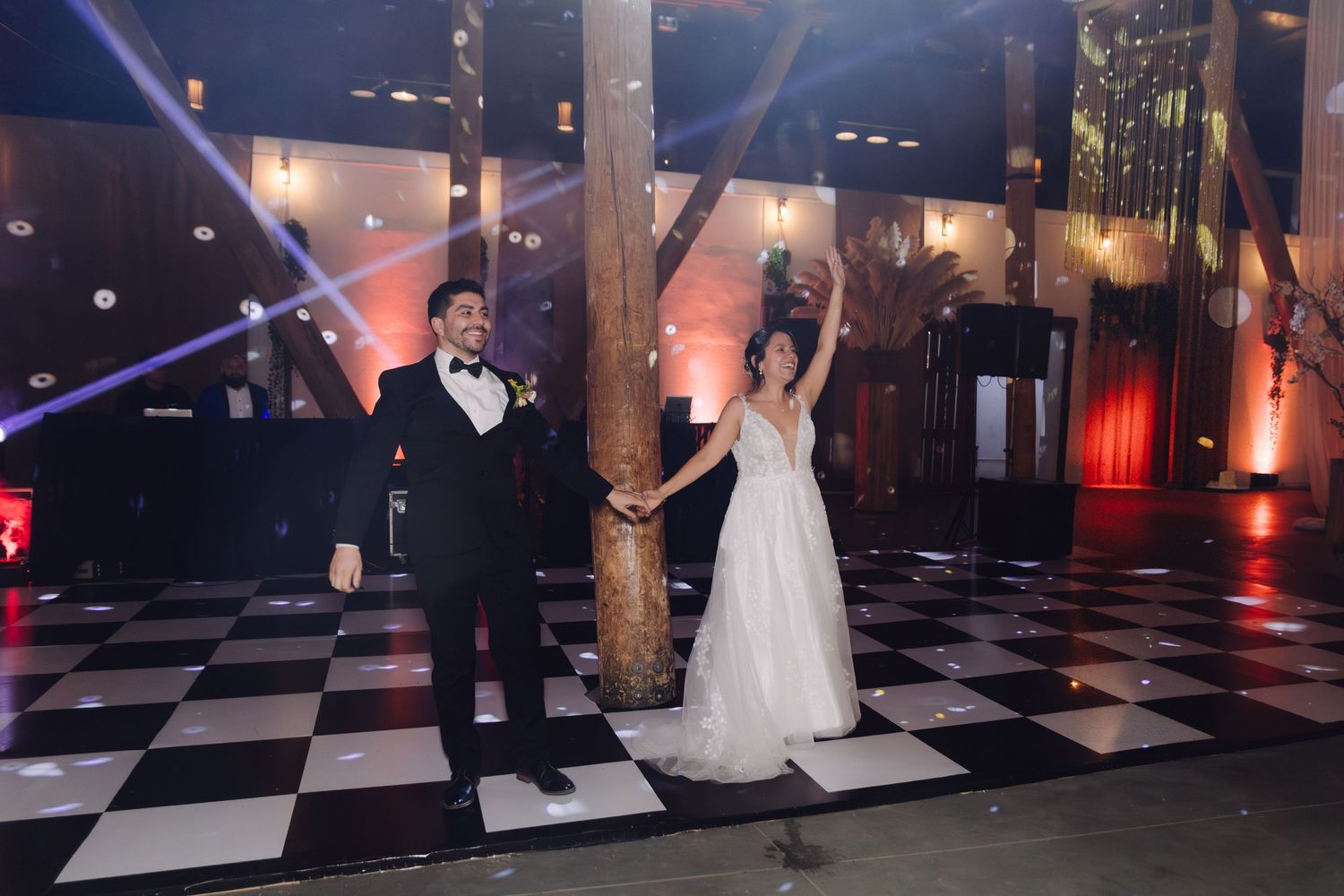 Bride and groom share first dance on black and white checkered dance floor with dramatic stage lighting.