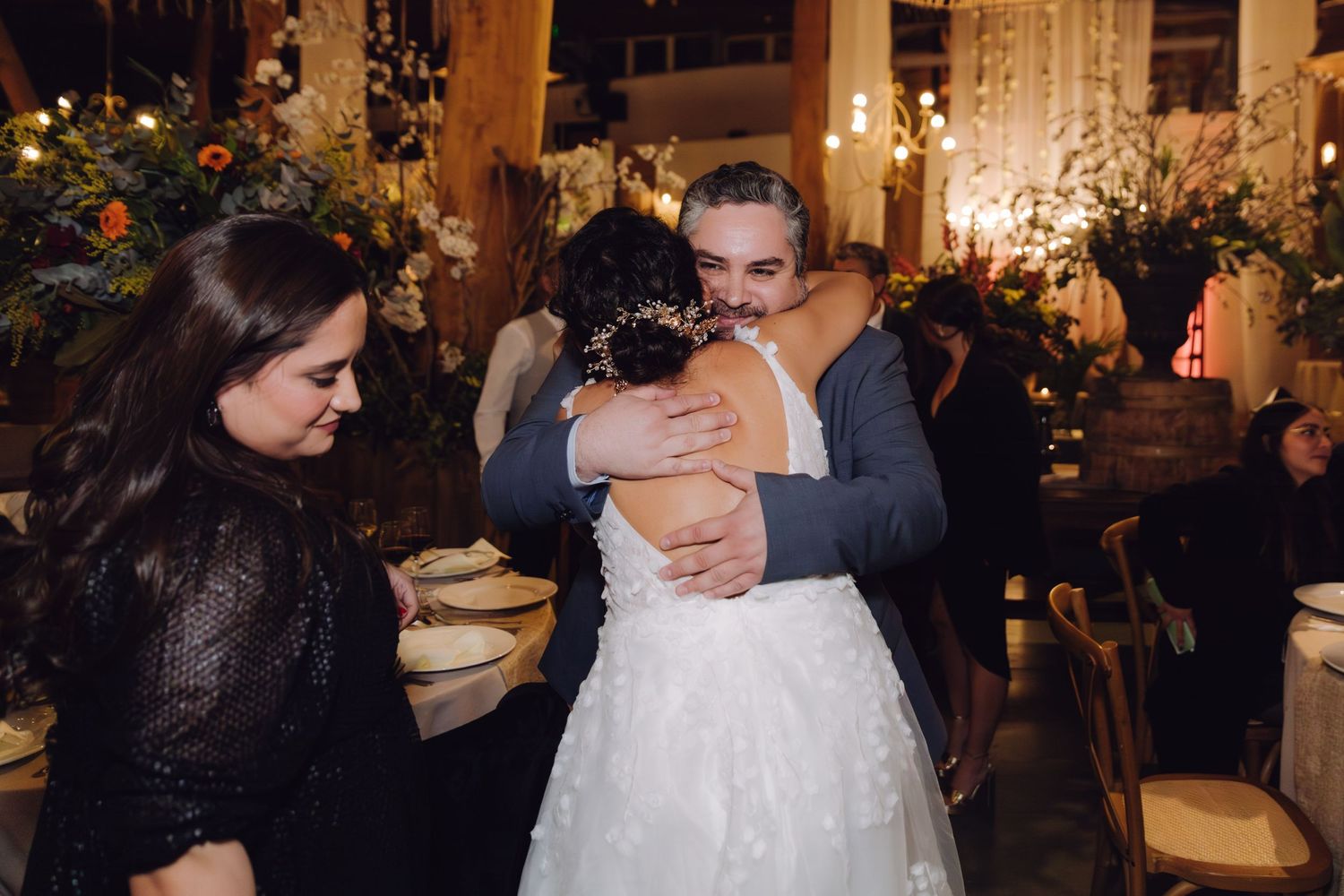 Bride receives warm hug from guest at romantic wedding reception with elegant floral decorations.