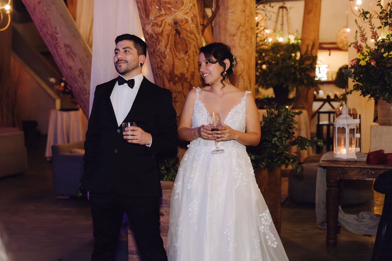 A bride and groom share a toast at their rustic indoor wedding reception with warm ambient lighting.