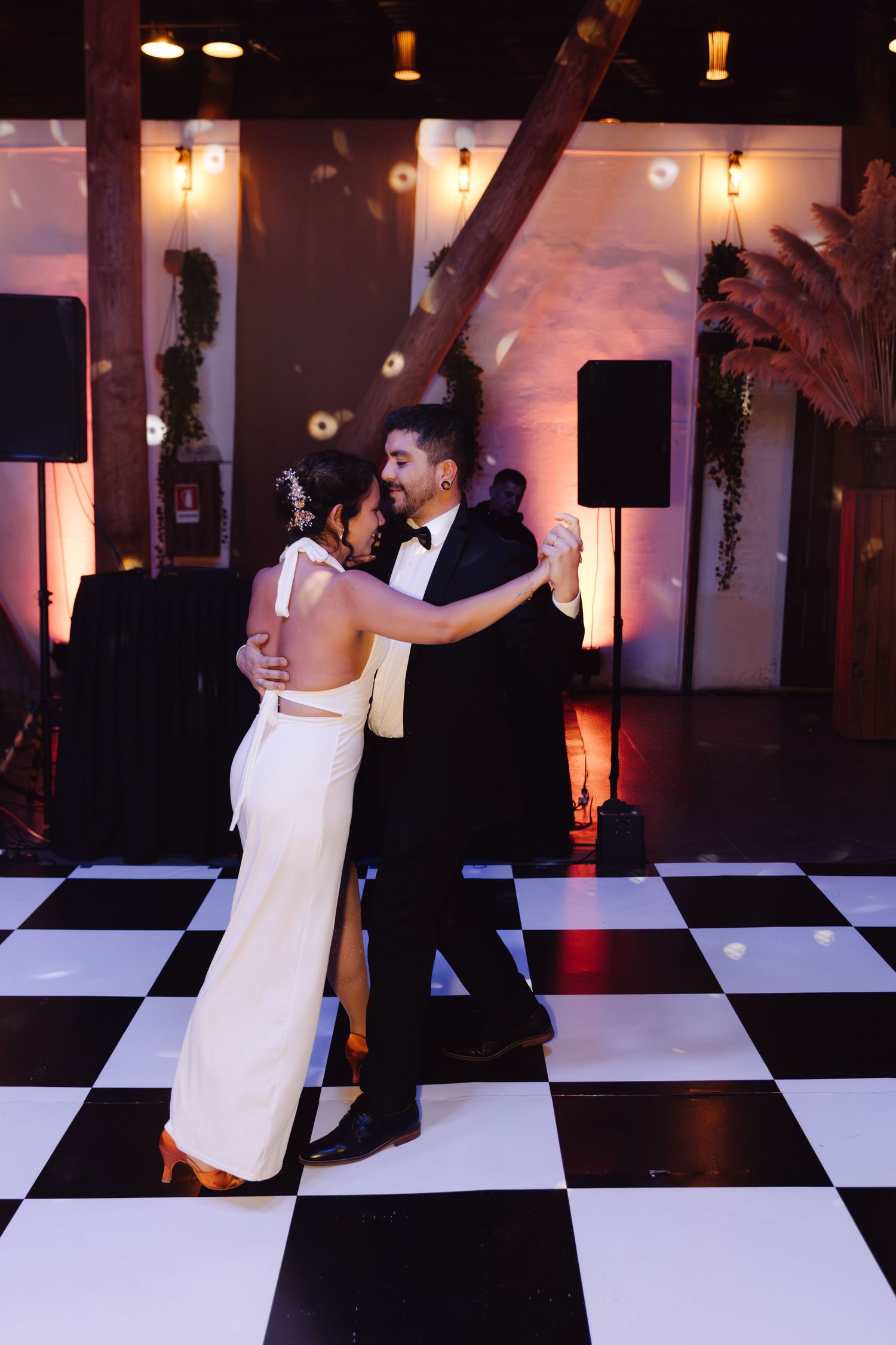 A bride and groom share their first dance on a black and white checkered dance floor at their wedding.