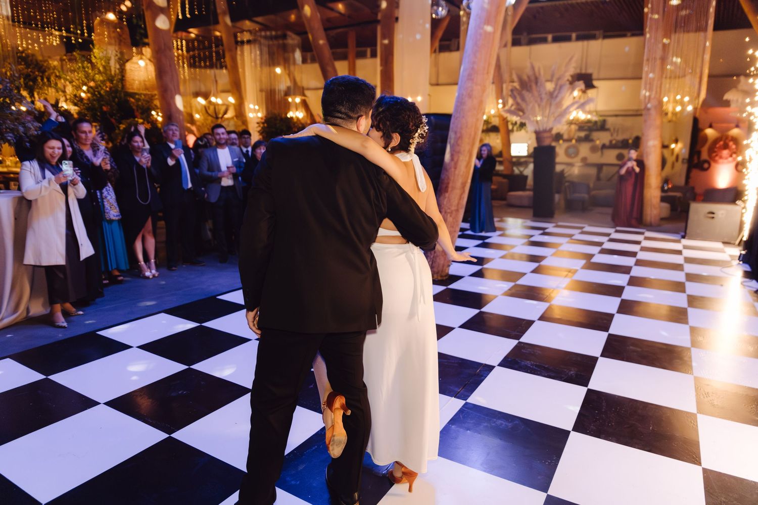 Wedding guests watch as the bride and groom dance on a black and white checkered dance floor.