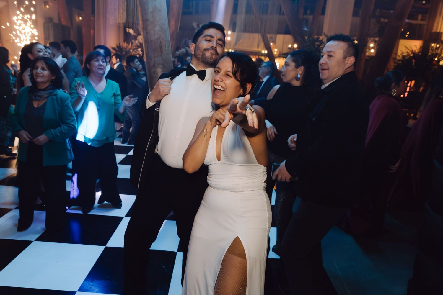 Bride in white gown and groom in tuxedo dancing joyfully at wedding reception.