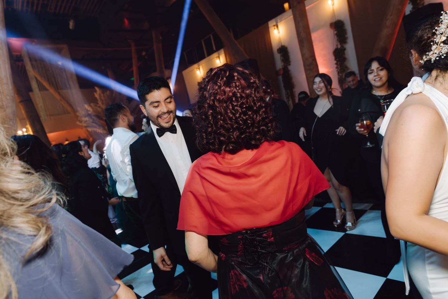 Man in tuxedo dancing with woman in red cape on checkered dance floor at wedding.