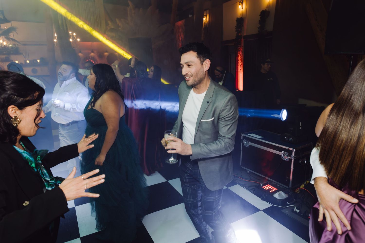 Man in gray suit holding wine glass socializing on dance floor at formal event.
