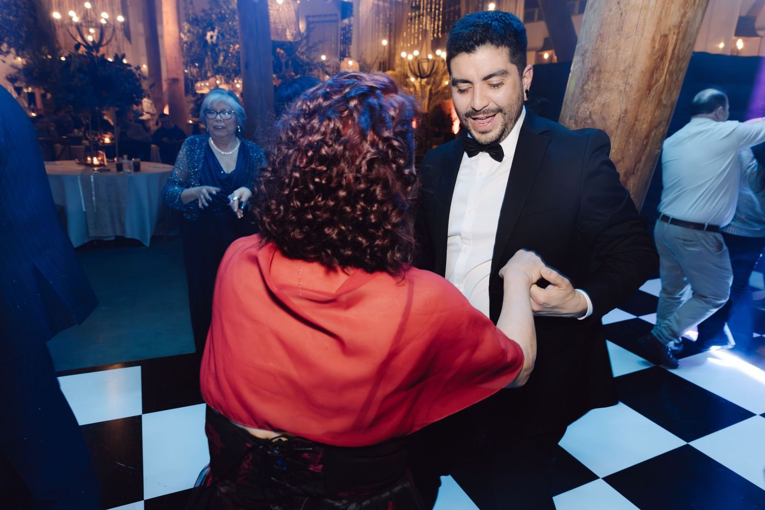 Man in tuxedo dancing with woman wearing red cape at formal wedding reception.