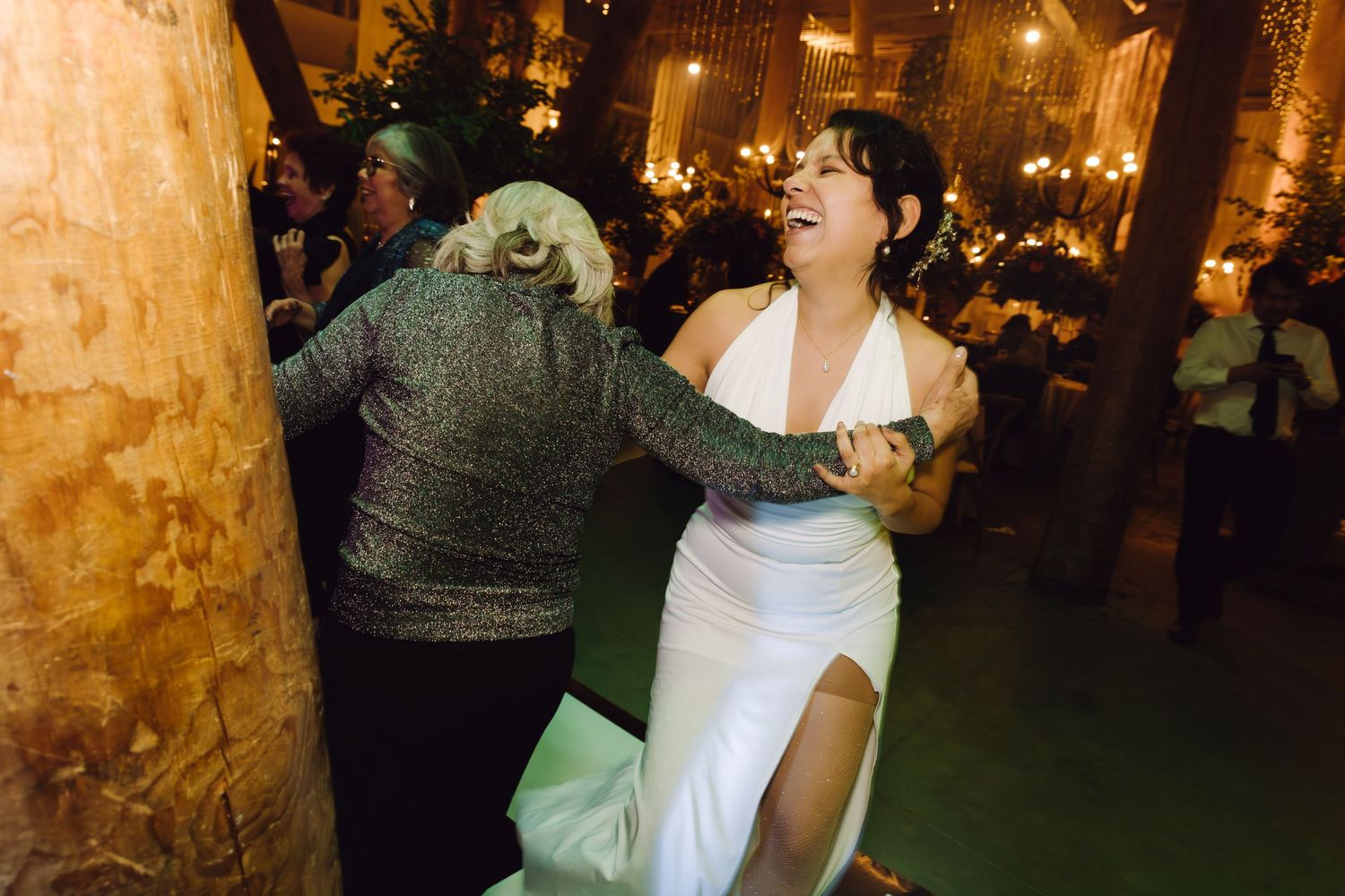 Bride in white halter gown laughing and dancing with guest at wedding reception.