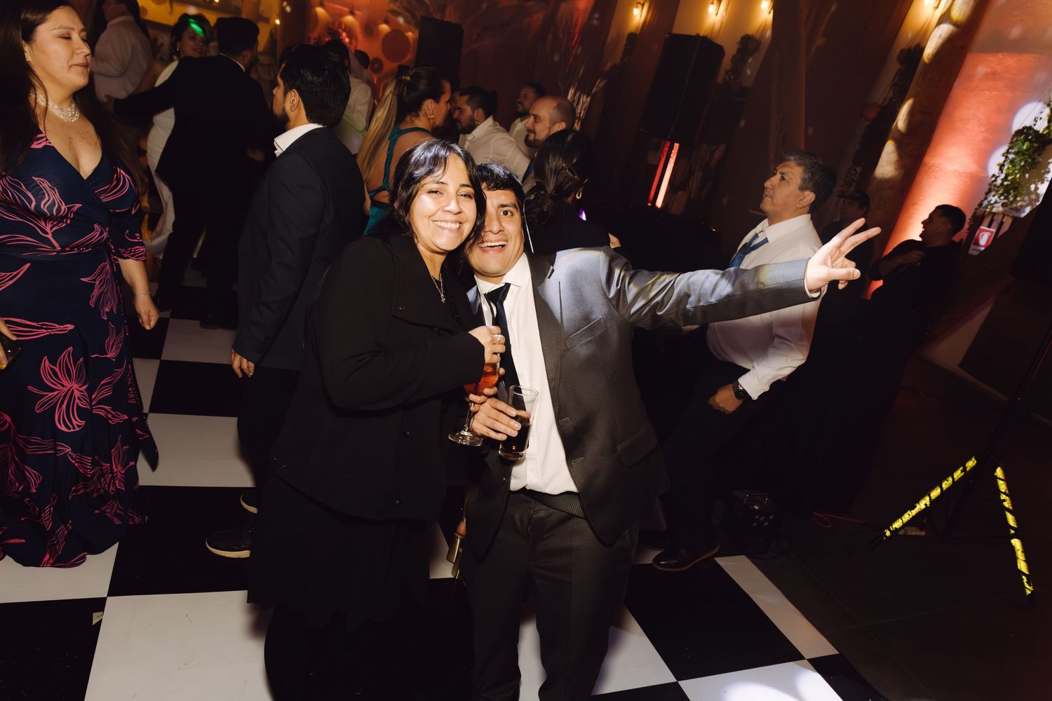 Two guests posing and smiling together on checkered dance floor at wedding reception.