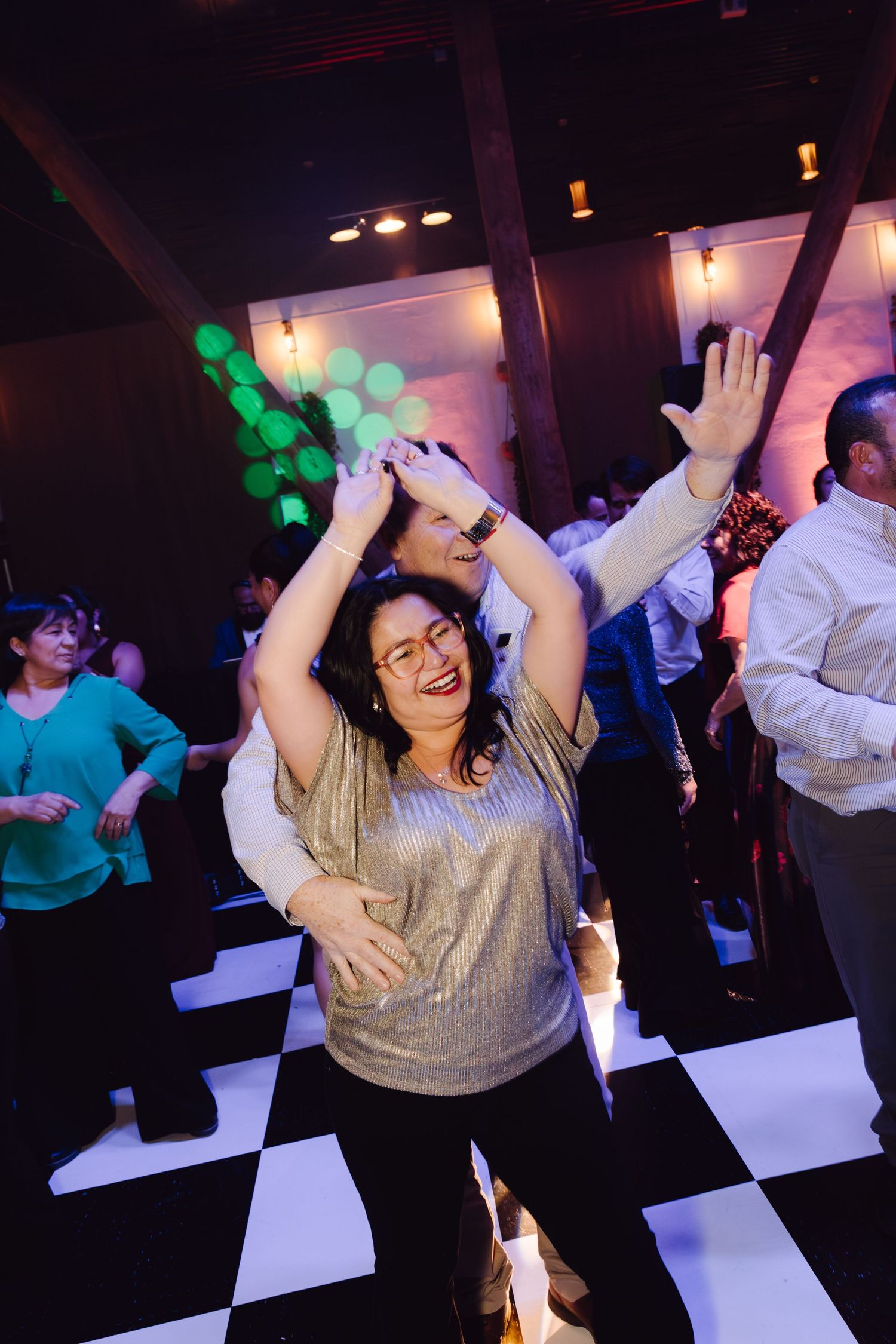 Woman in silver top dancing joyfully on checkered dance floor at a lively party event.