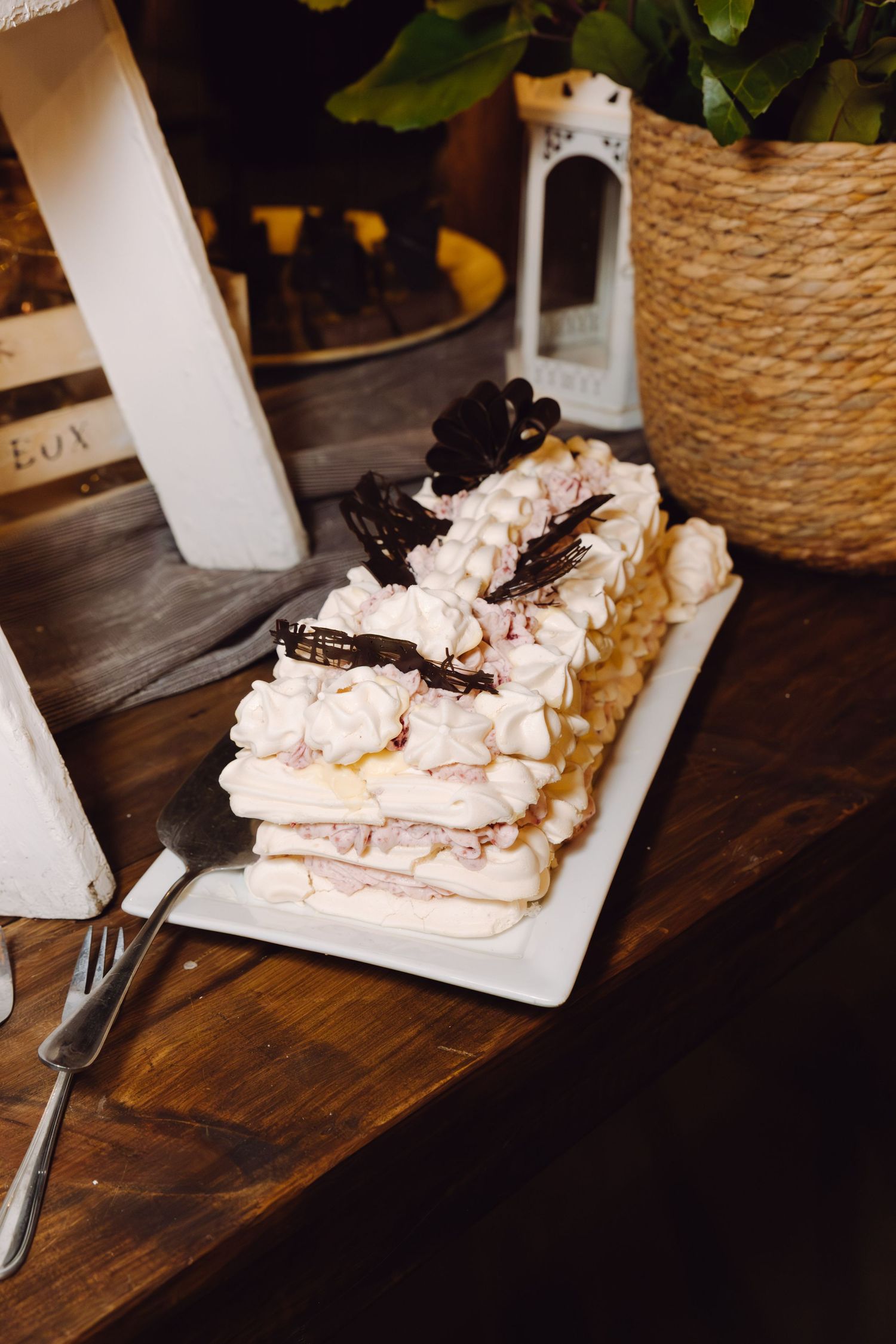 Elegant layered meringue cake with chocolate decorations on white platter at wedding reception.