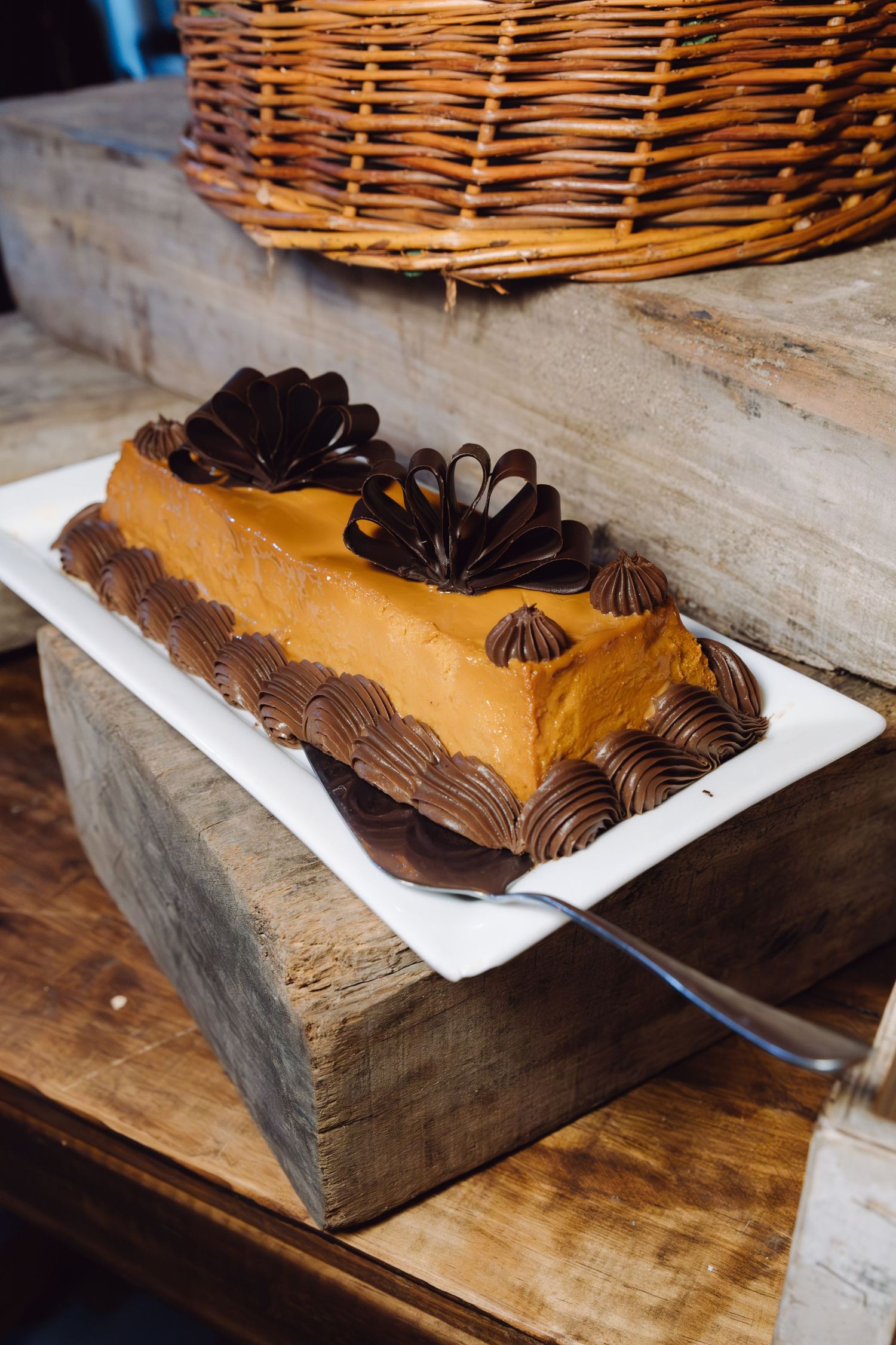 Caramel mousse cake with chocolate flower decorations on white plate at wedding dessert table.