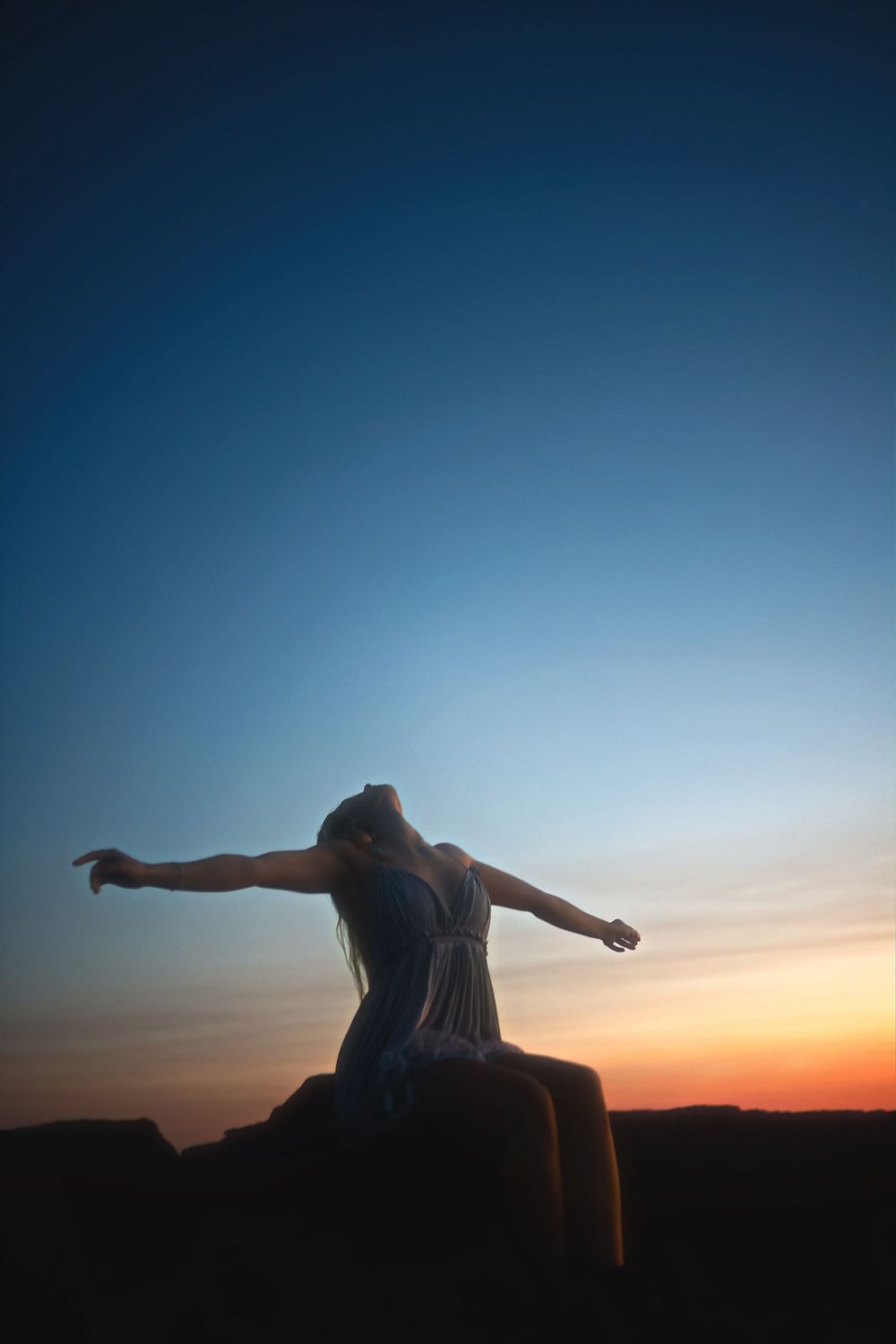 Silhouette of a person with outstretched arms against a vibrant sunset sky over mountain ridges.