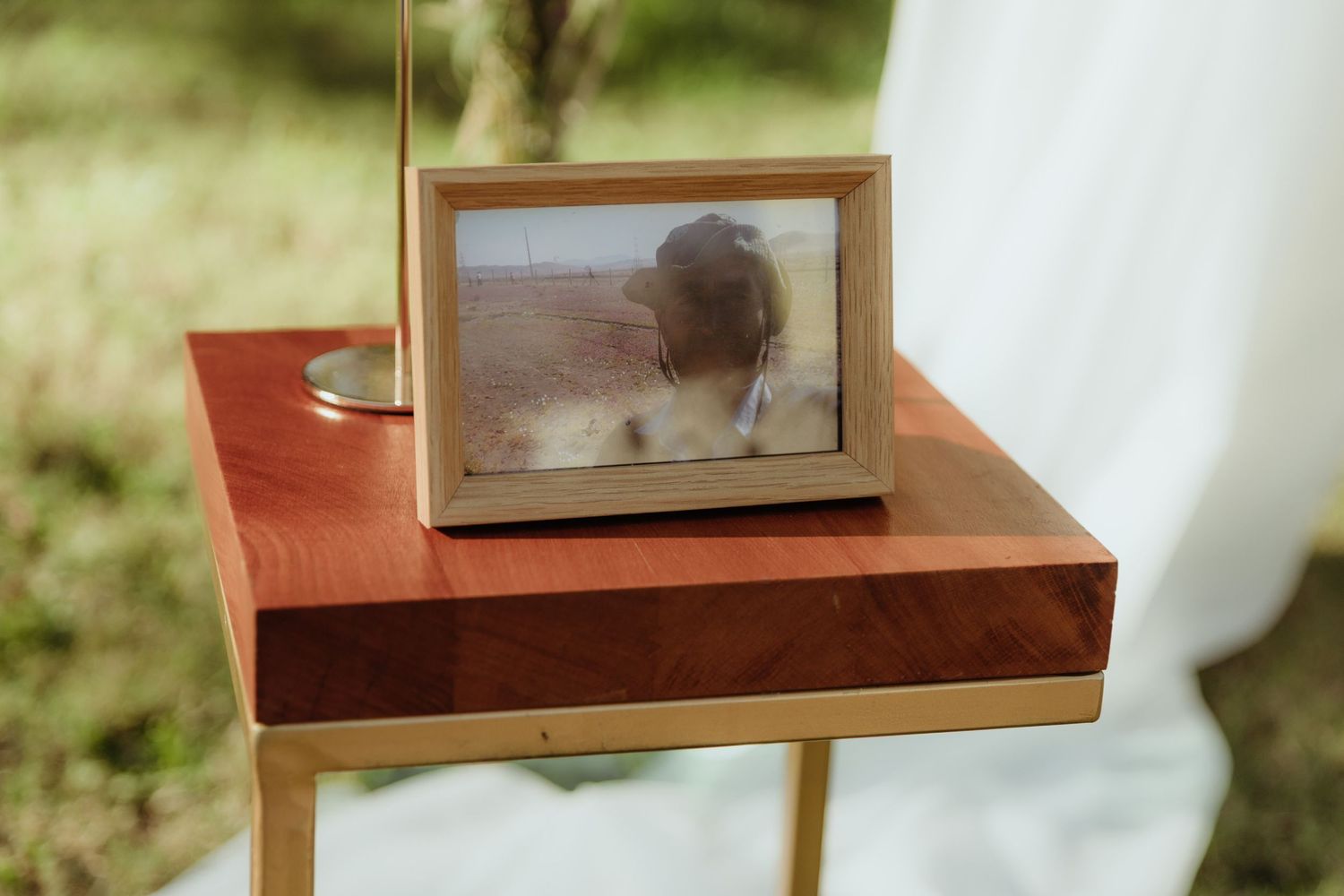 Gold-framed photo of a person displayed on a wooden side table at an outdoor wedding ceremony.