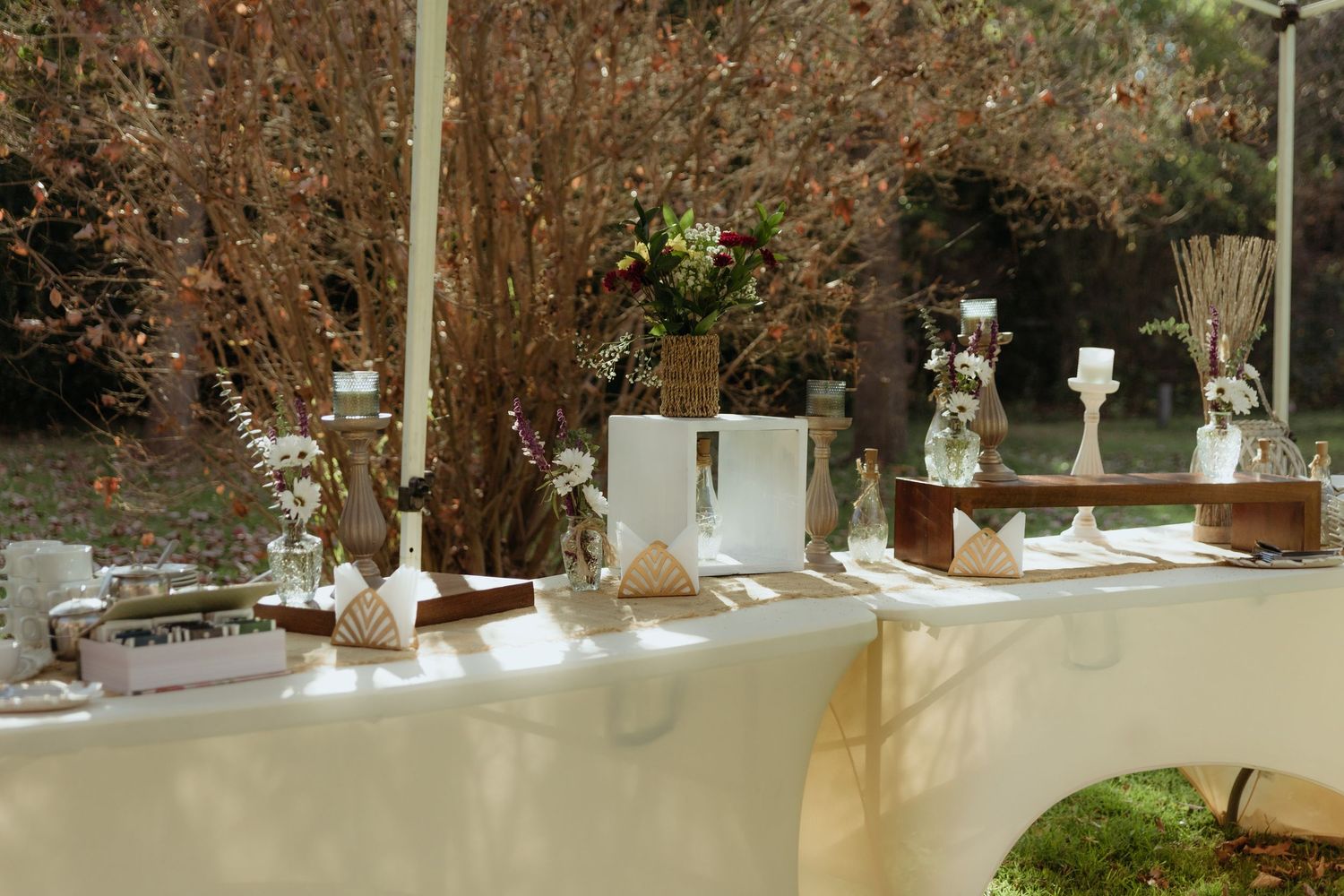 Elegant outdoor wedding reception table with white linen, floral arrangements, vases, and decorative accents.