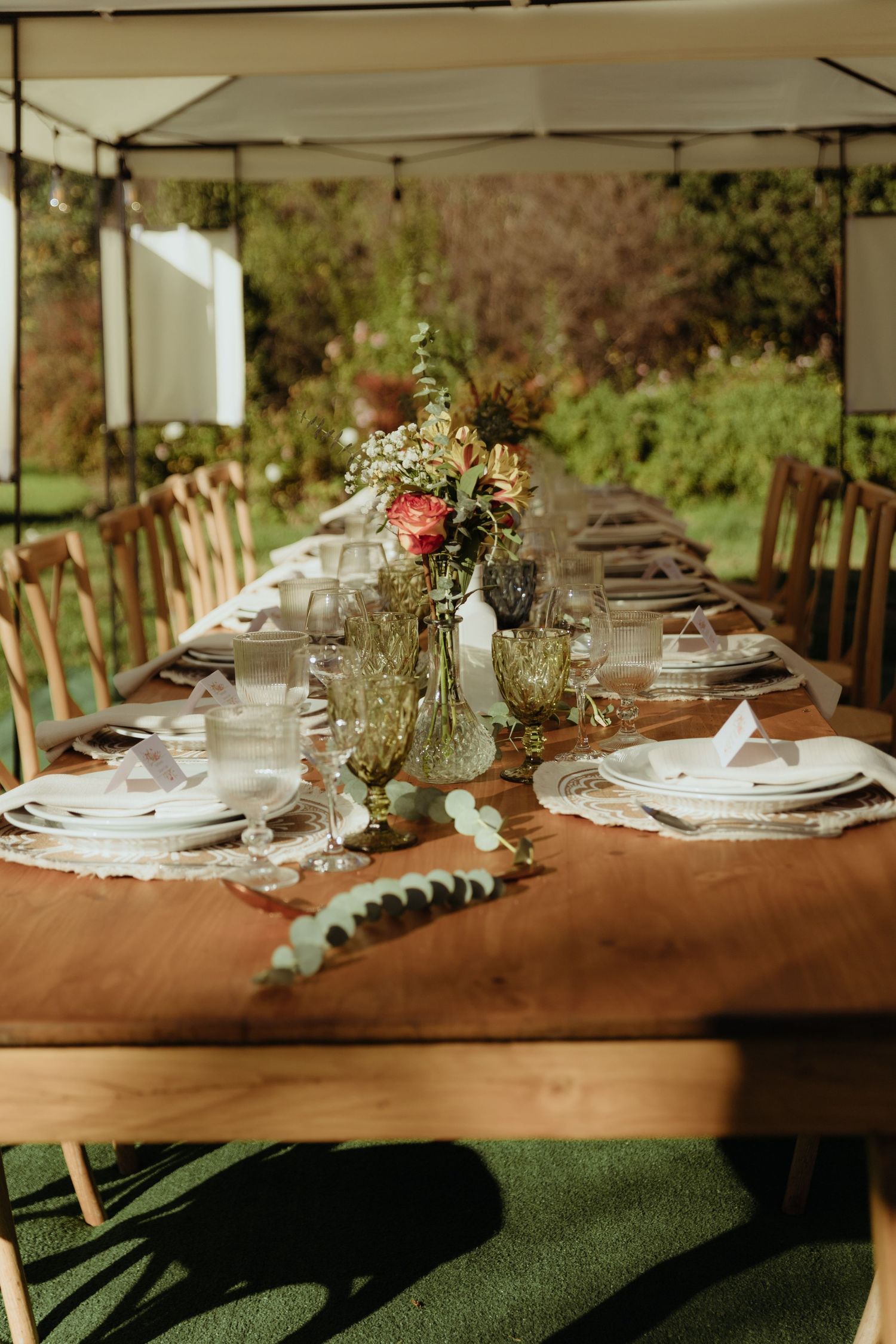 Rustic wooden wedding reception table elegantly set with white plates, glassware, and floral centerpieces.