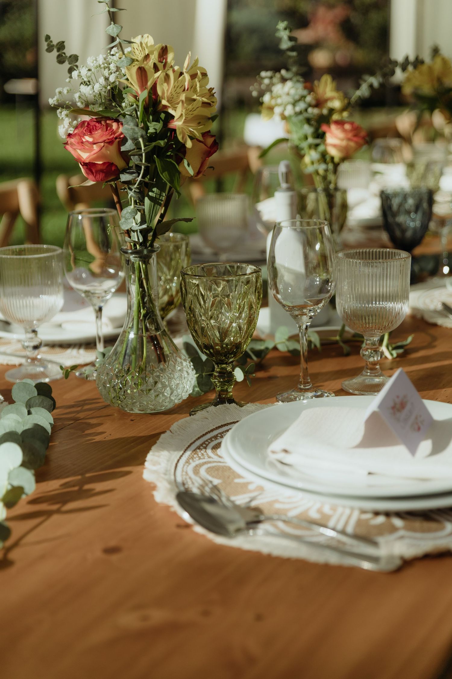Close-up of rustic wedding table setting with green glassware, white plates, and fresh floral centerpieces.