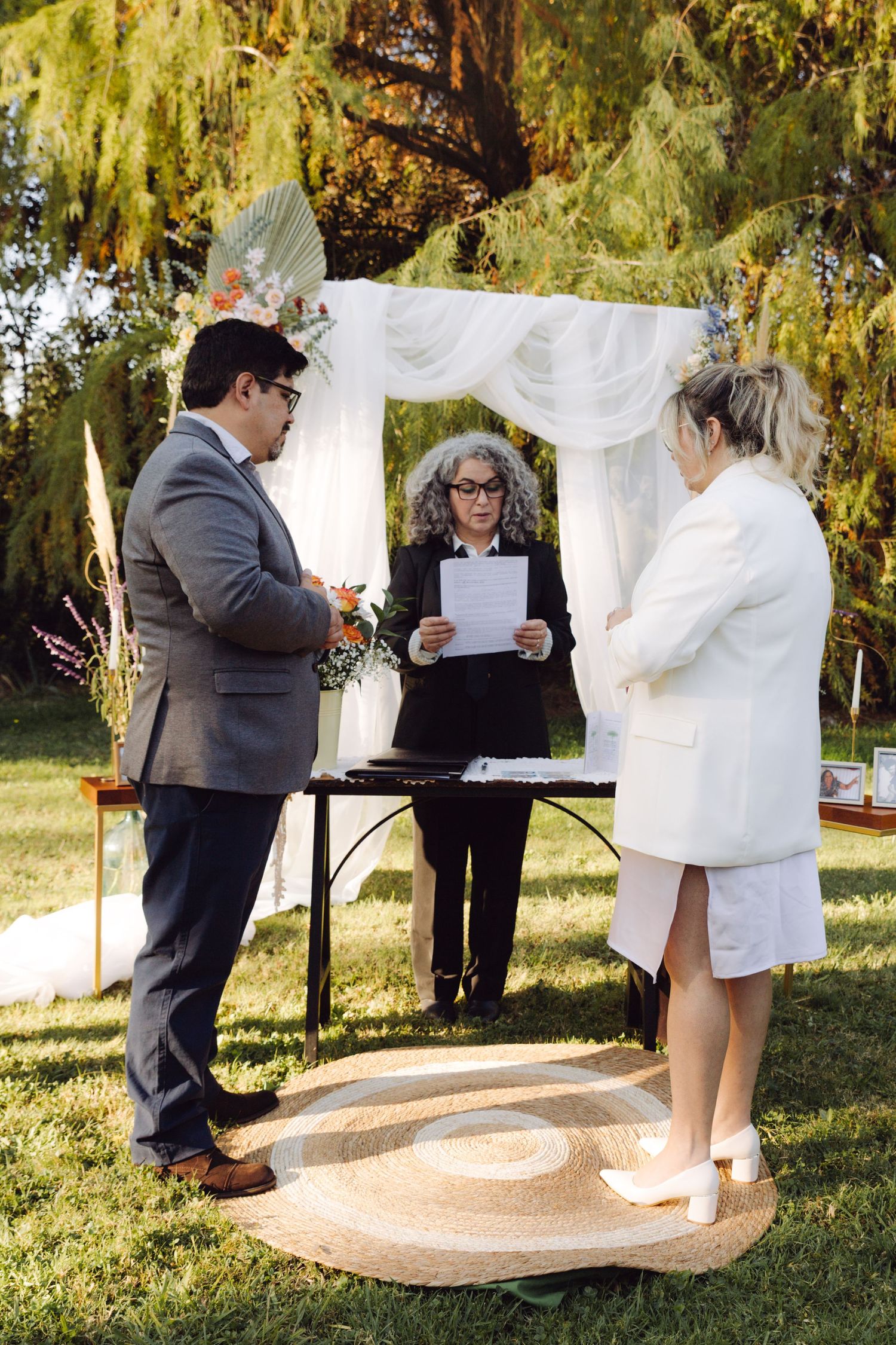 Bride and groom standing before officiant during elegant outdoor wedding ceremony on grass.