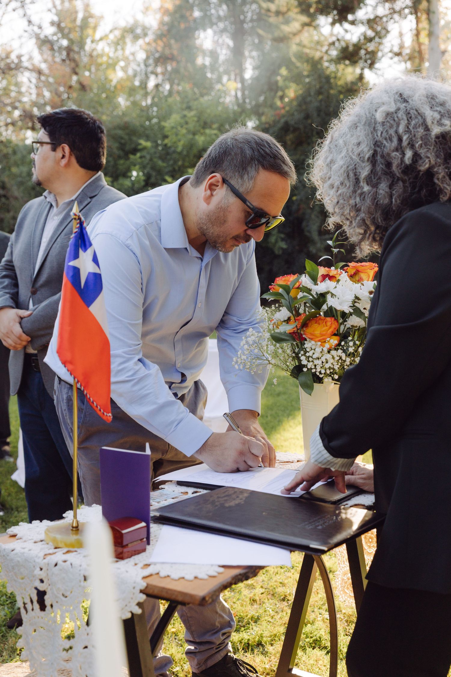 Wedding witness signing official marriage register at outdoor ceremony with Chilean flag.