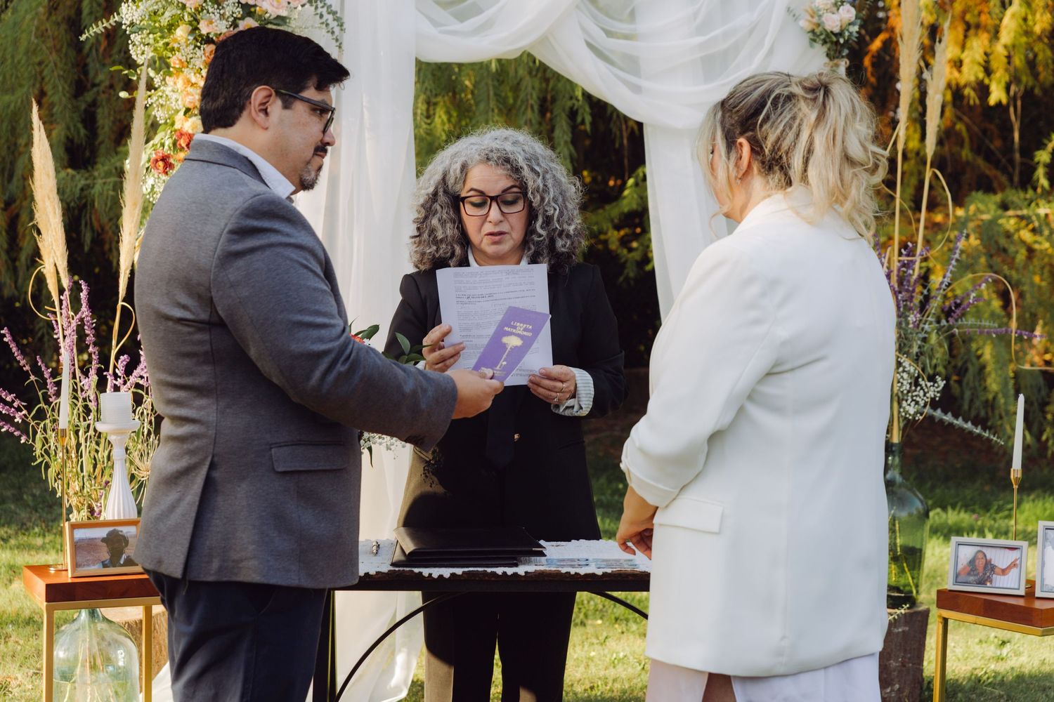 Wedding officiant reading from purple booklet during outdoor garden marriage ceremony.