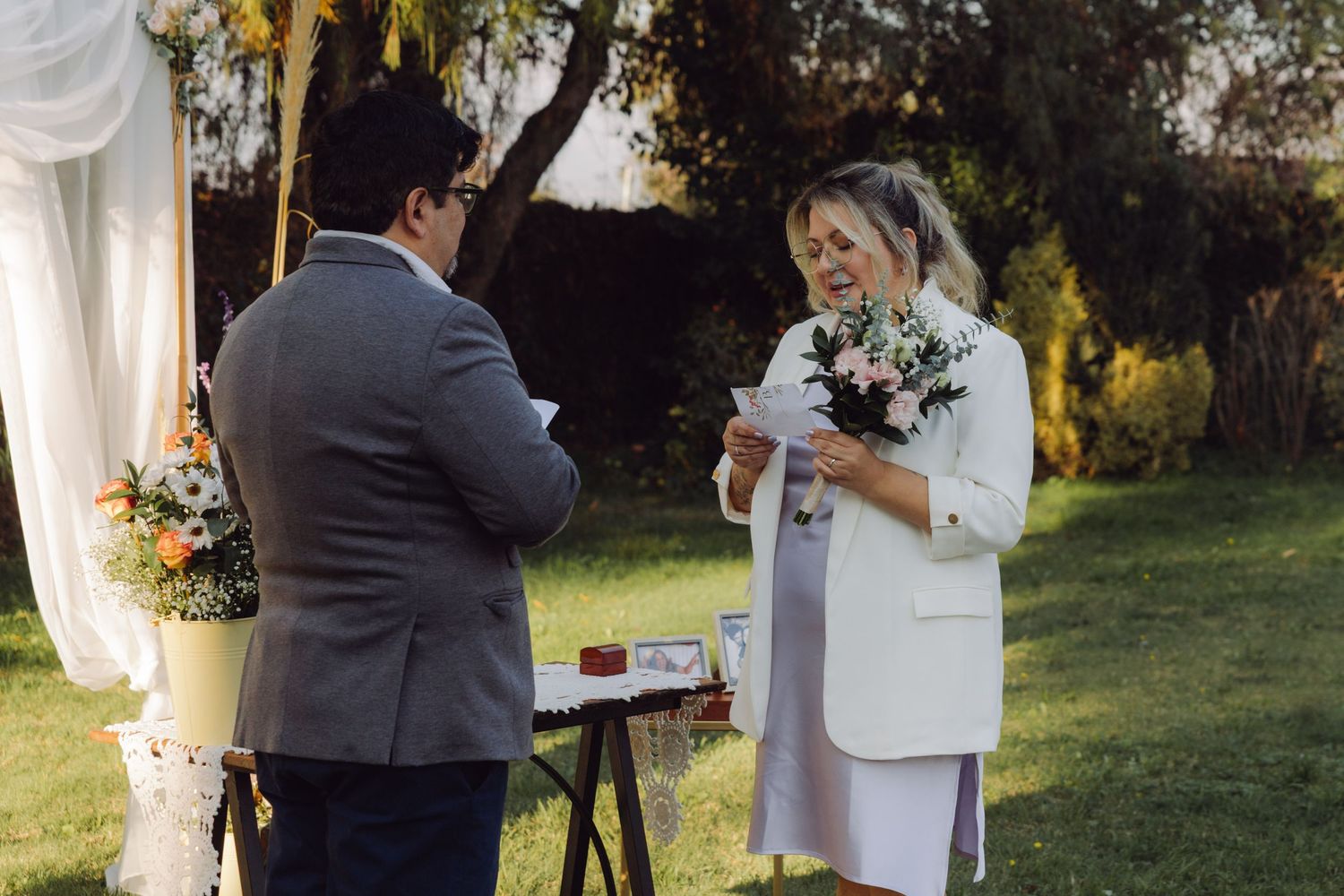 Bride reading heartfelt vows from paper to groom at outdoor garden wedding ceremony.